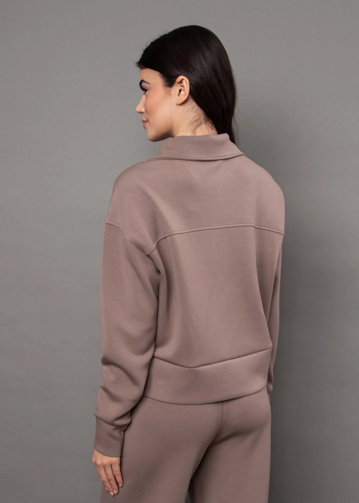 Back view of a dusty rose soft knit zip-up top featuring a structured collar, horizontal back seam, and ribbed hem for comfort.