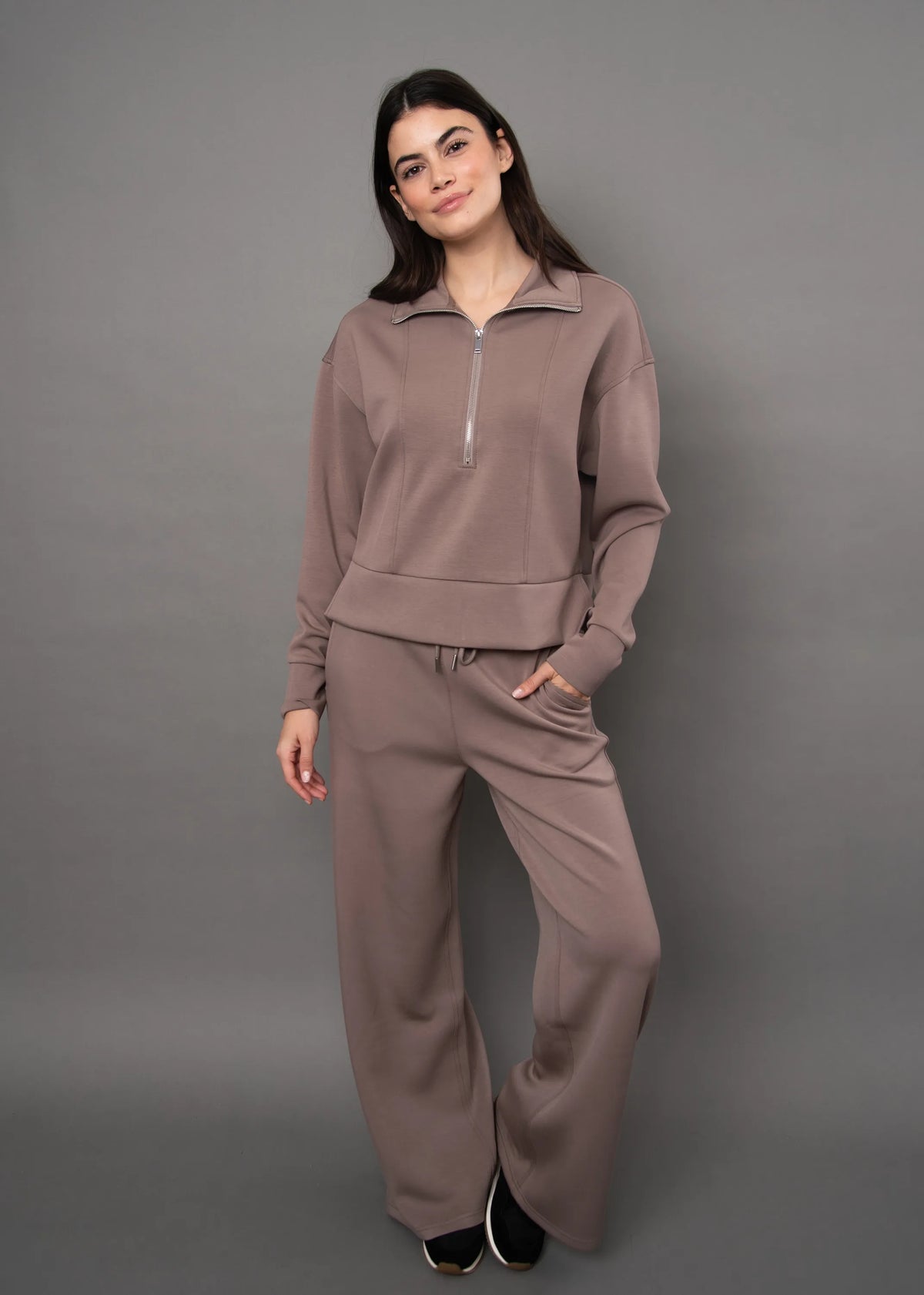 Model wearing a brown soft knit quarter-zip top and matching wide-leg pants set against a grey background.
