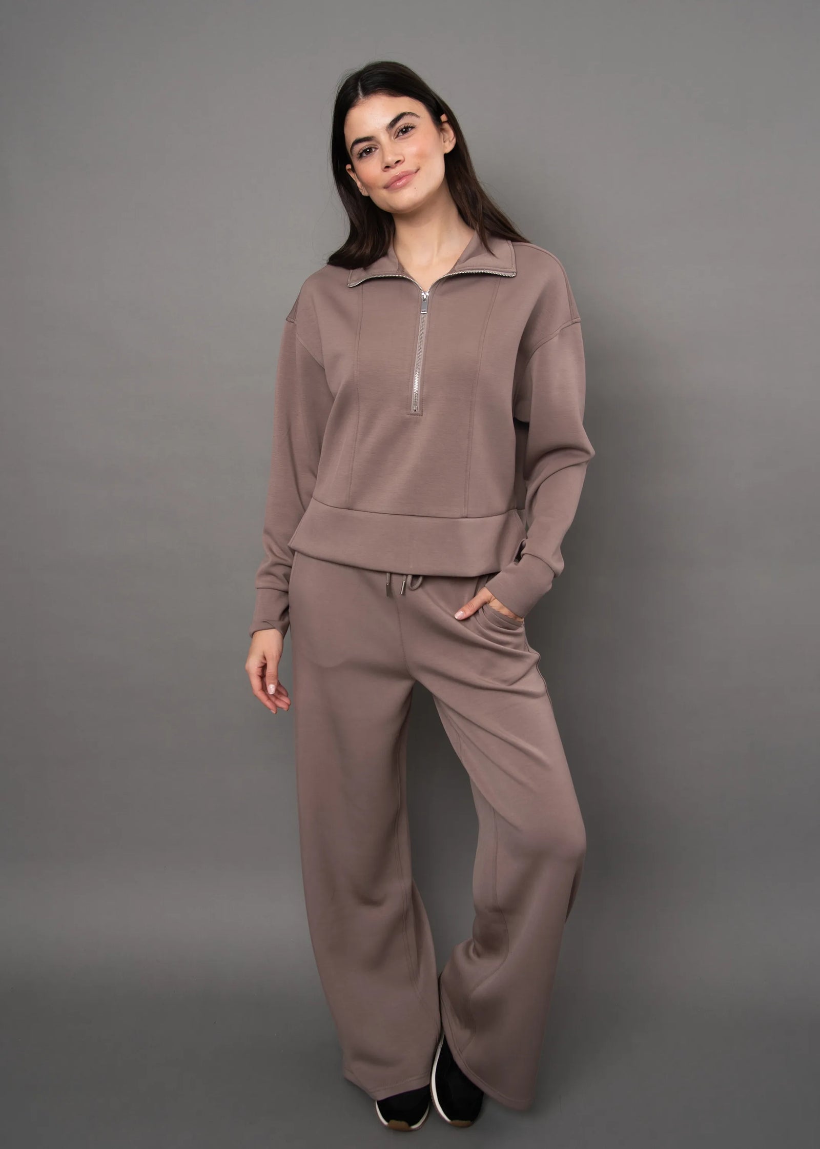Model wearing a brown soft knit quarter-zip top and matching wide-leg pants set against a grey background.