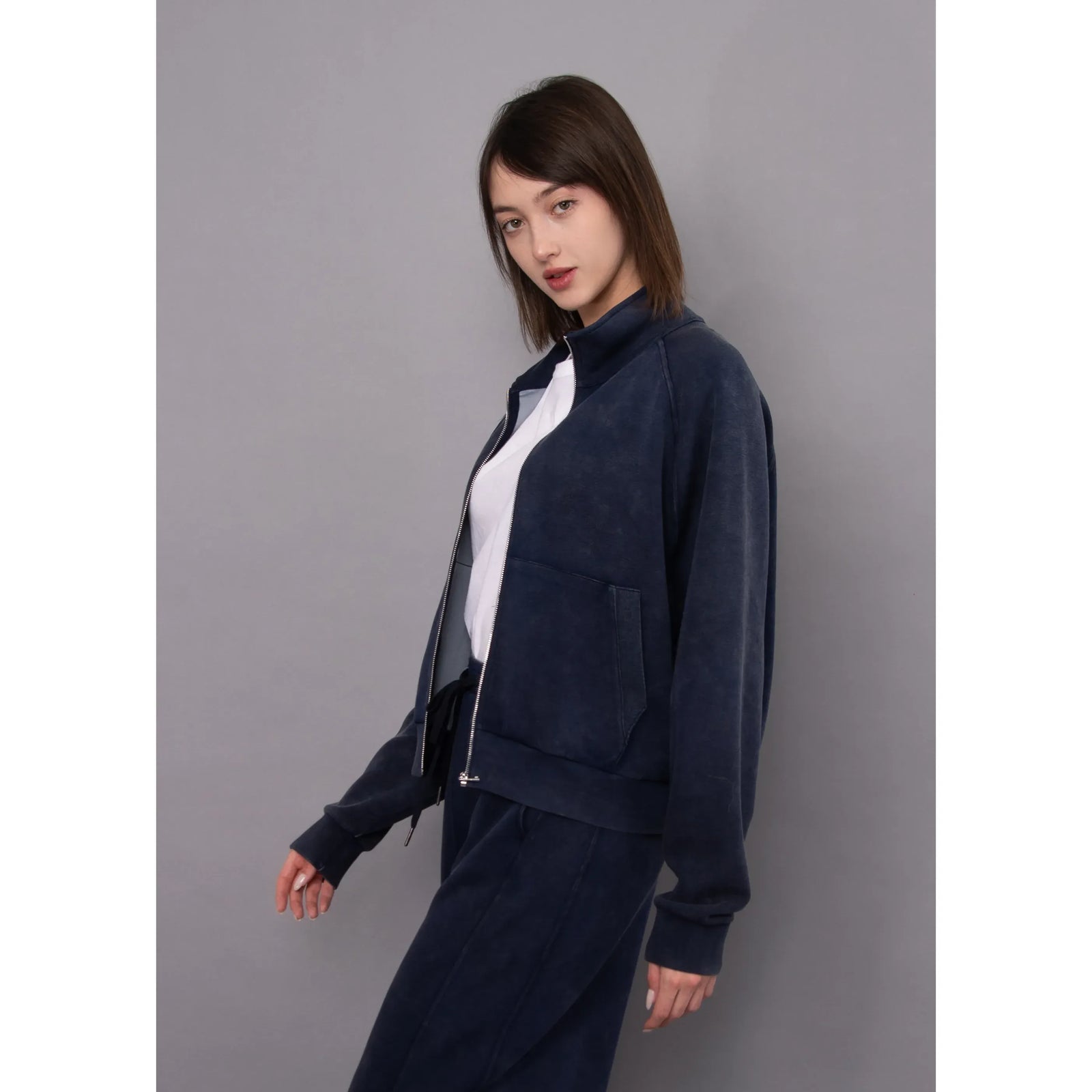 Model wearing a navy mineral wash soft knit zip-up top with a stand collar, front pocket, and white tee underneath.