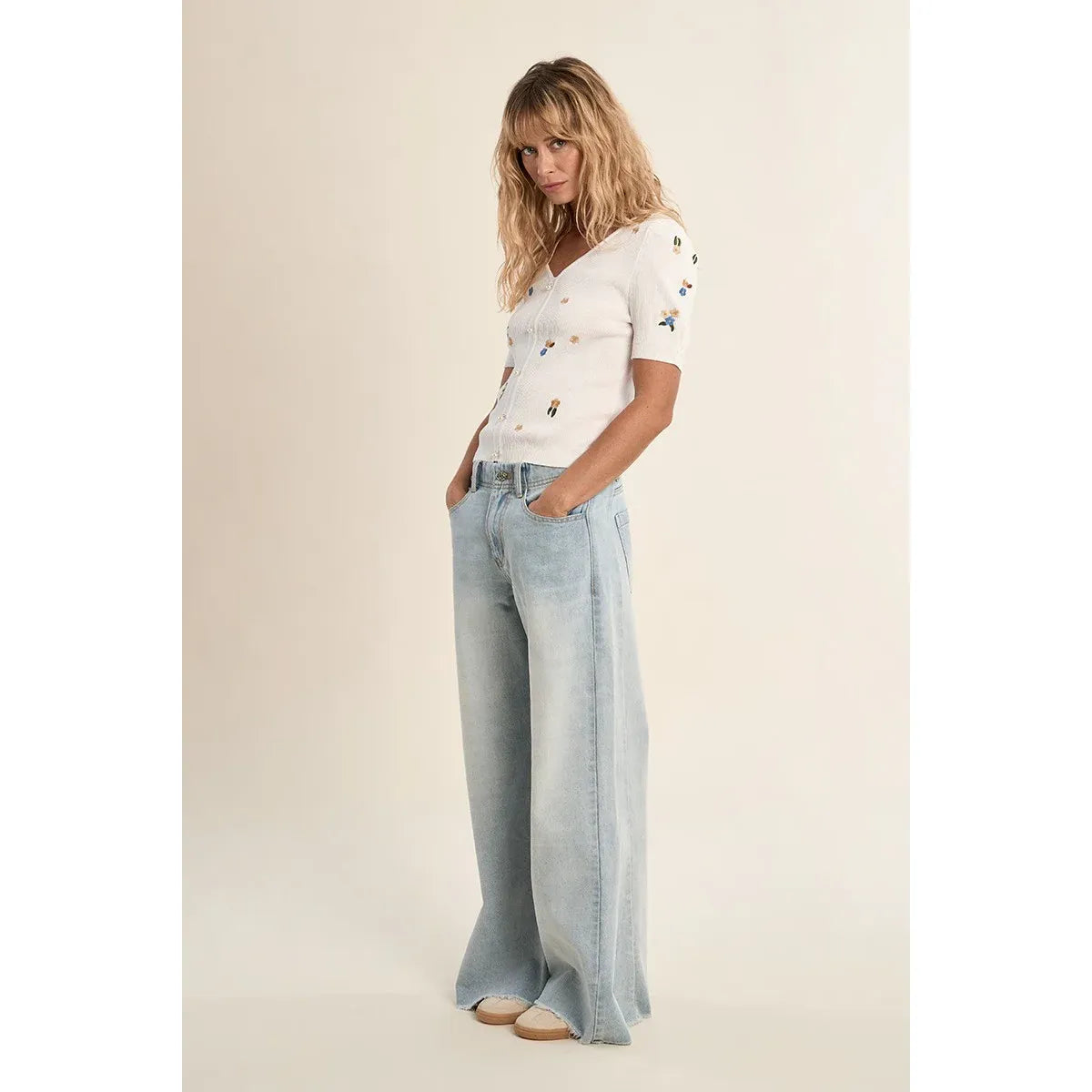 Molly Bracken white embroidered short-sleeve sweater with floral details and V-neck, light denim wide-leg jeans.