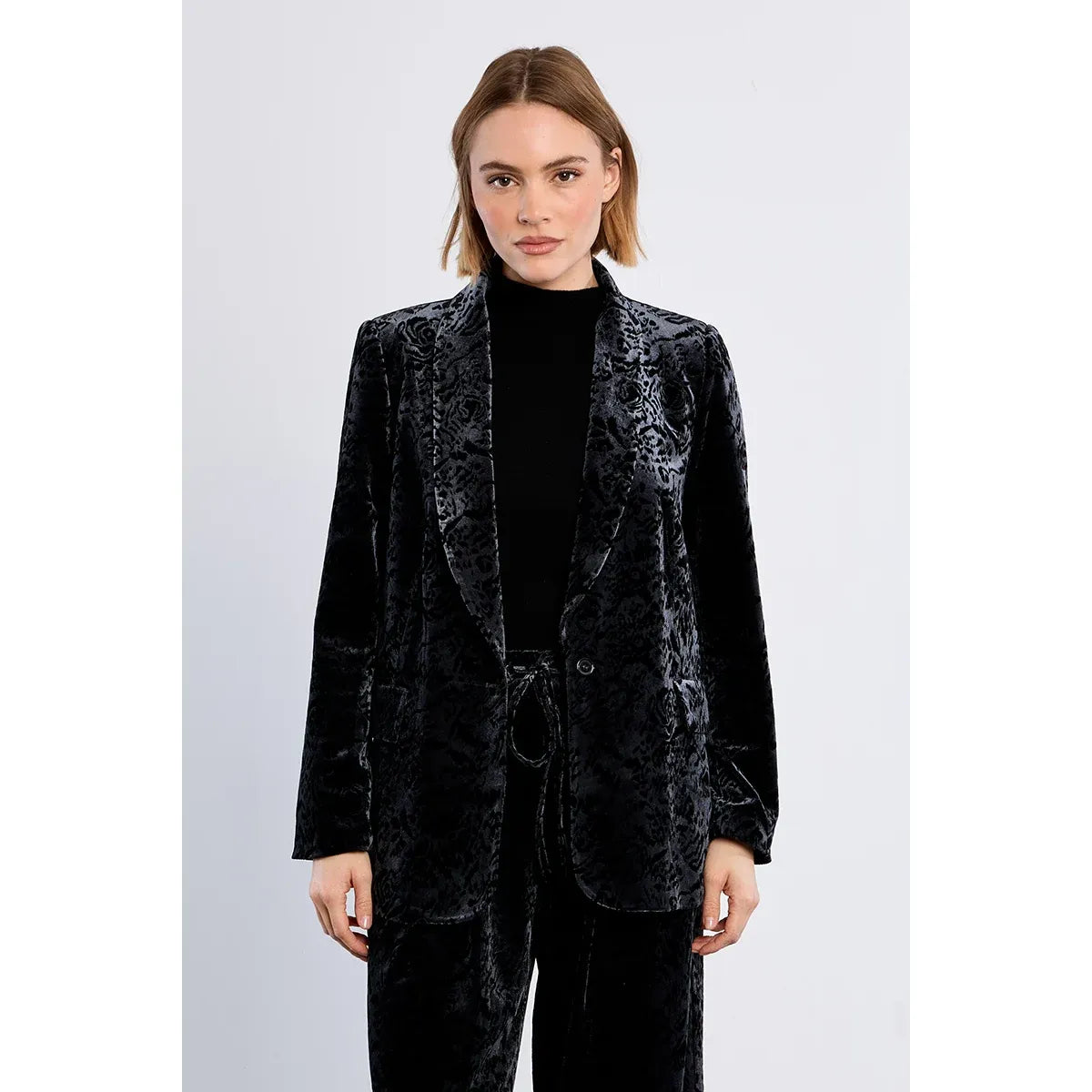 Black floral velvet blazer with a straight fit and single button closure, styled over a black top for a dressed-up casual look.