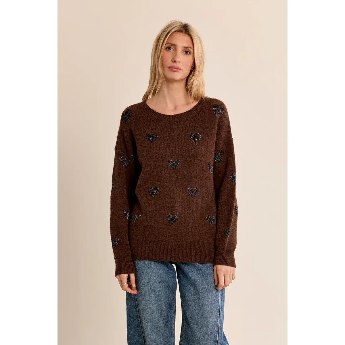 Brown knit sweater with glittery heart pattern, round neckline, and relaxed fit worn with blue jeans.