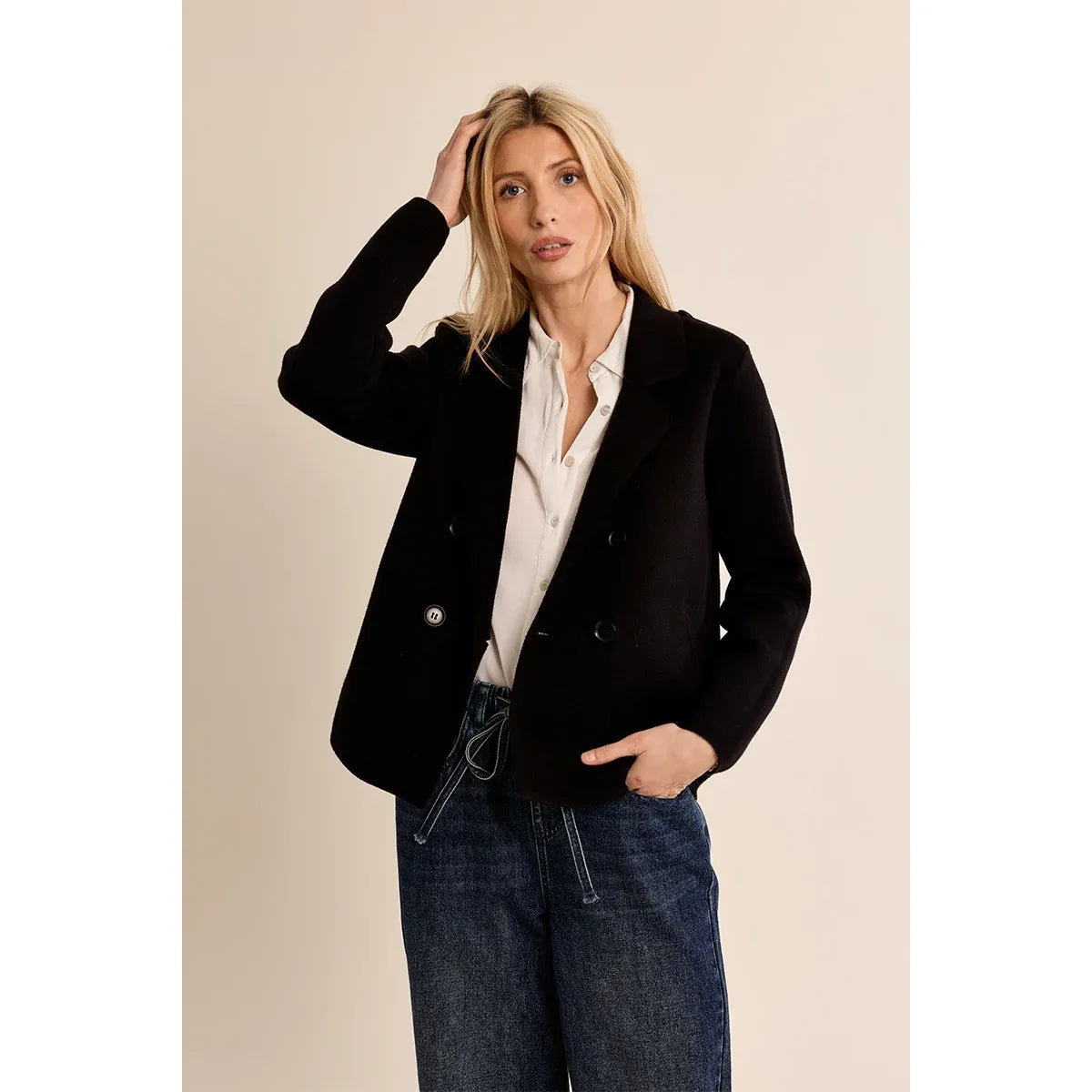 Woman wearing a black cropped knit blazer with double-breasted buttons over a white shirt and blue jeans.