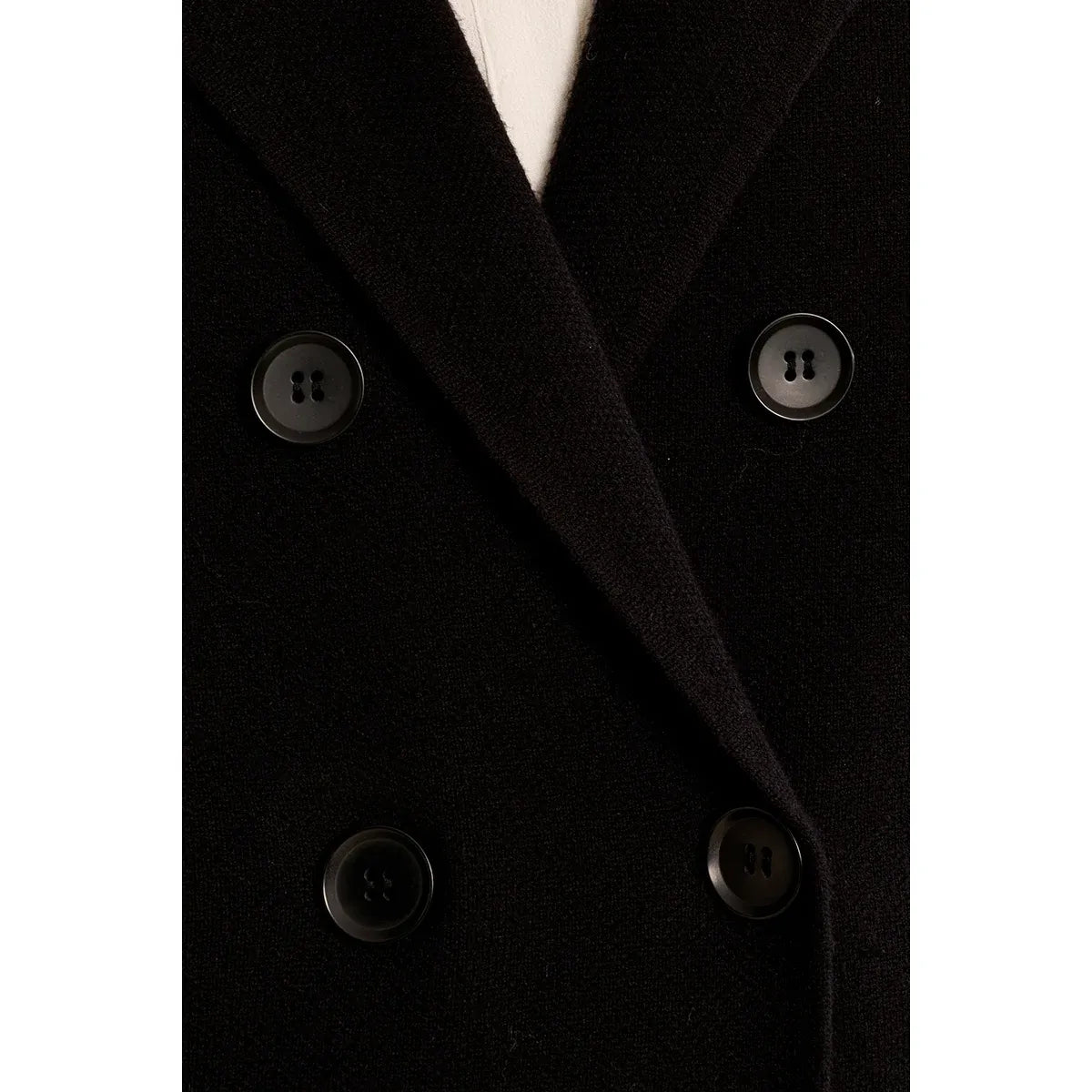 Close-up of a black knit jacket featuring a structured collar and four dark buttons on a chic cropped blazer coat.
