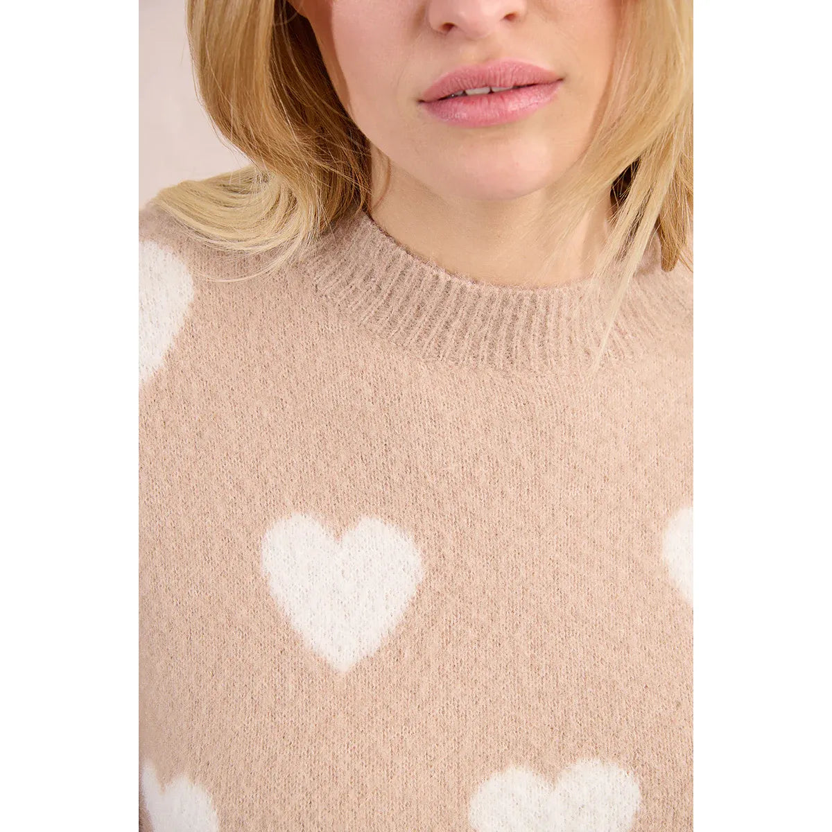 Woman wearing a soft heather pink Molly Bracken Heart Sweater with white heart motifs and a round neckline.