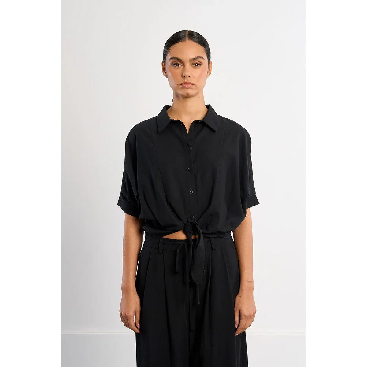 Black Molly Bracken knotted blouse with front knot, shirt collar, mid-length sleeves, paired with waist-tie pants.