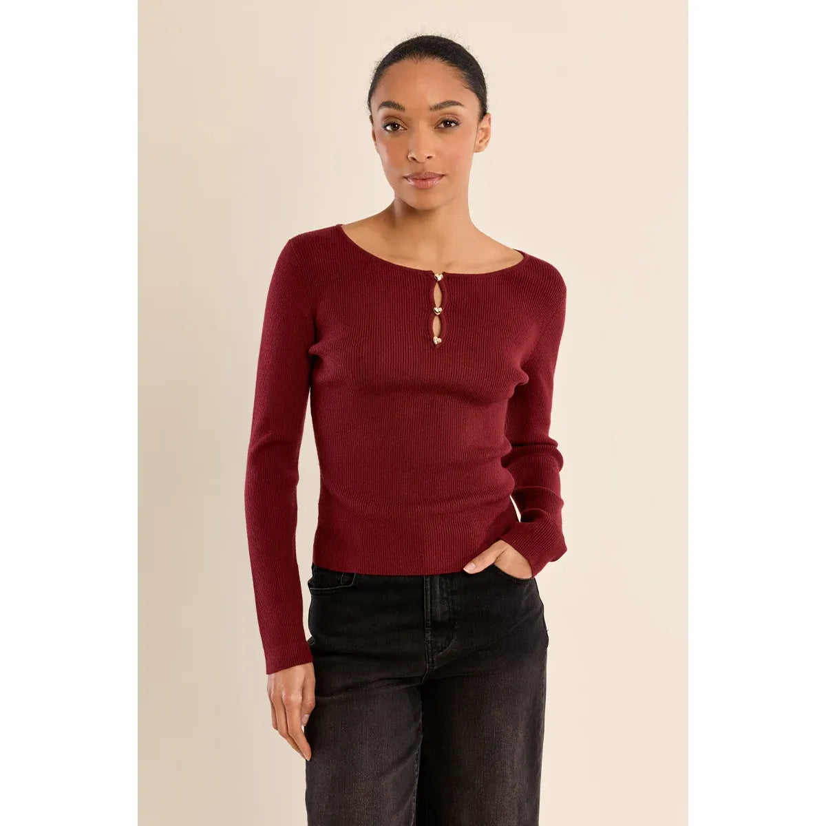 Burgundy fine ribbed sweater with round neck and gold heart-shaped buttons, styled with black jeans.