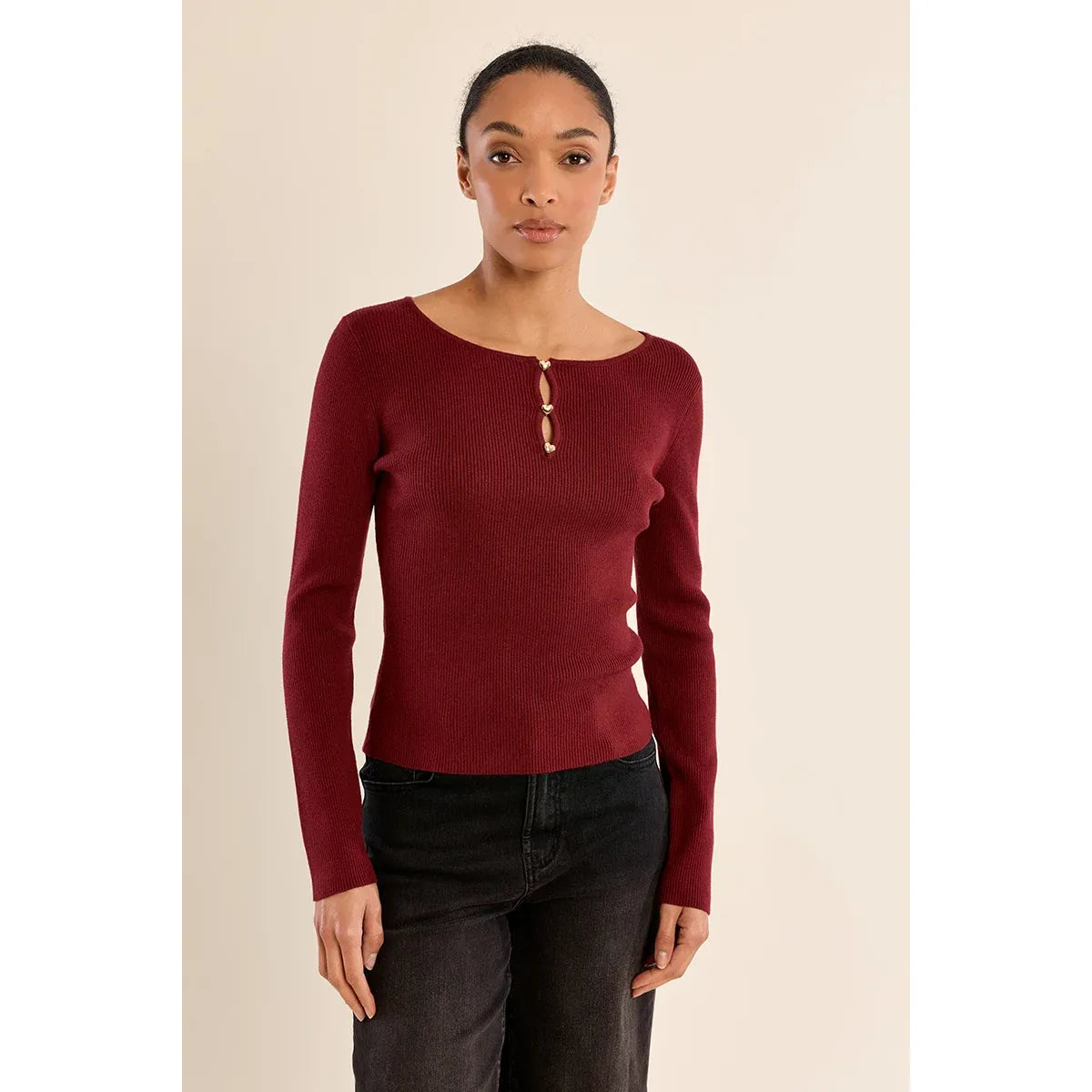 Burgundy fine ribbed sweater with round neck and gold heart-shaped buttons, styled with black jeans.