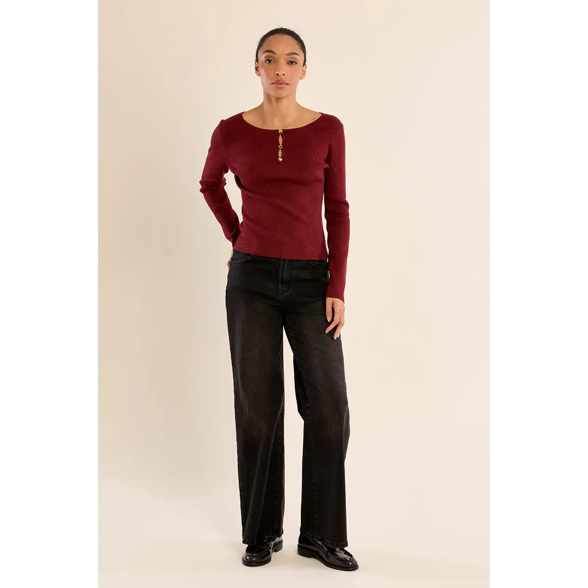 Model wears a maroon fine ribbed sweater with heart-shaped buttons at the round neck, paired with black wide-leg jeans.