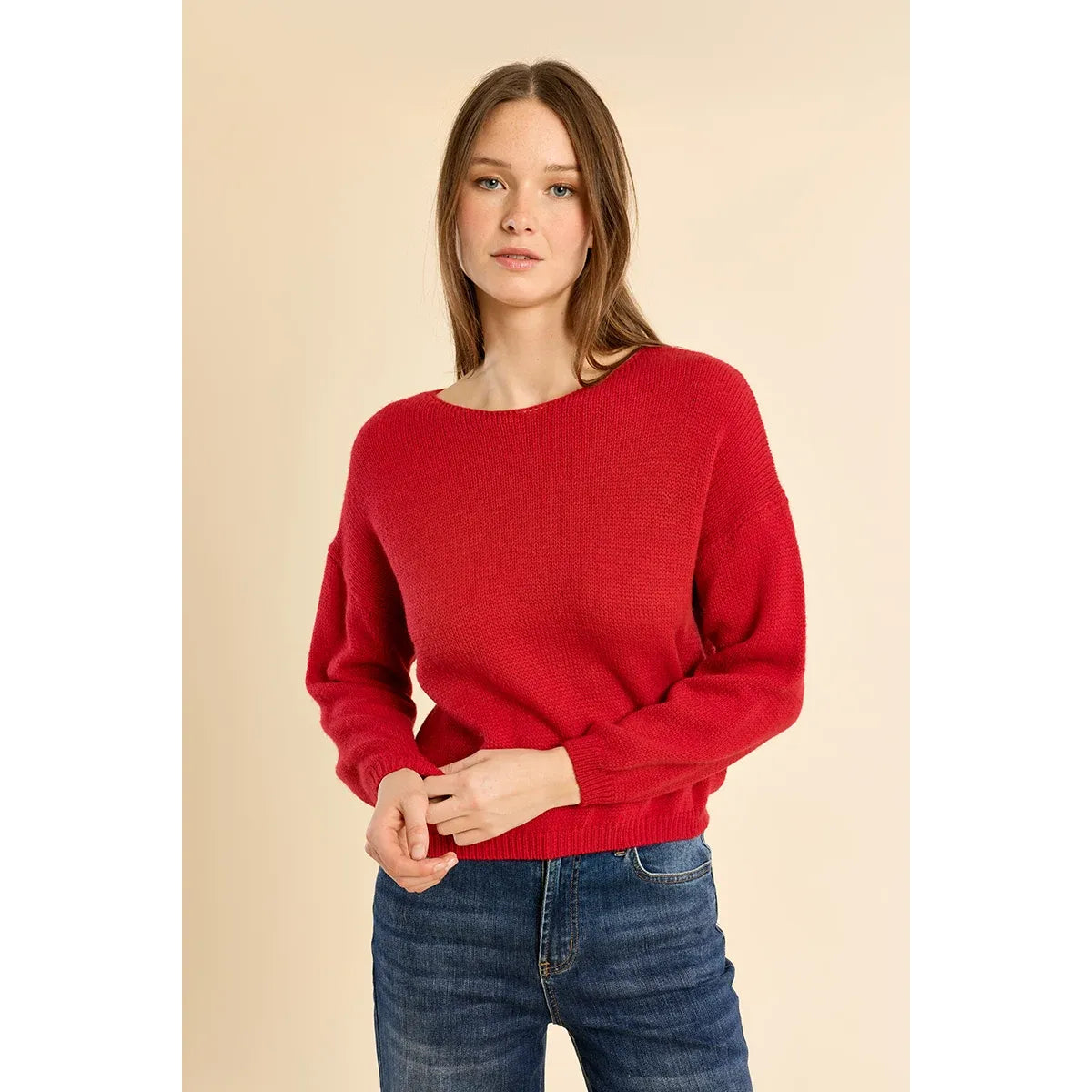 Red round neck knit sweater with low armholes and ribbed trim at collar, cuffs, and waist, styled with blue jeans.