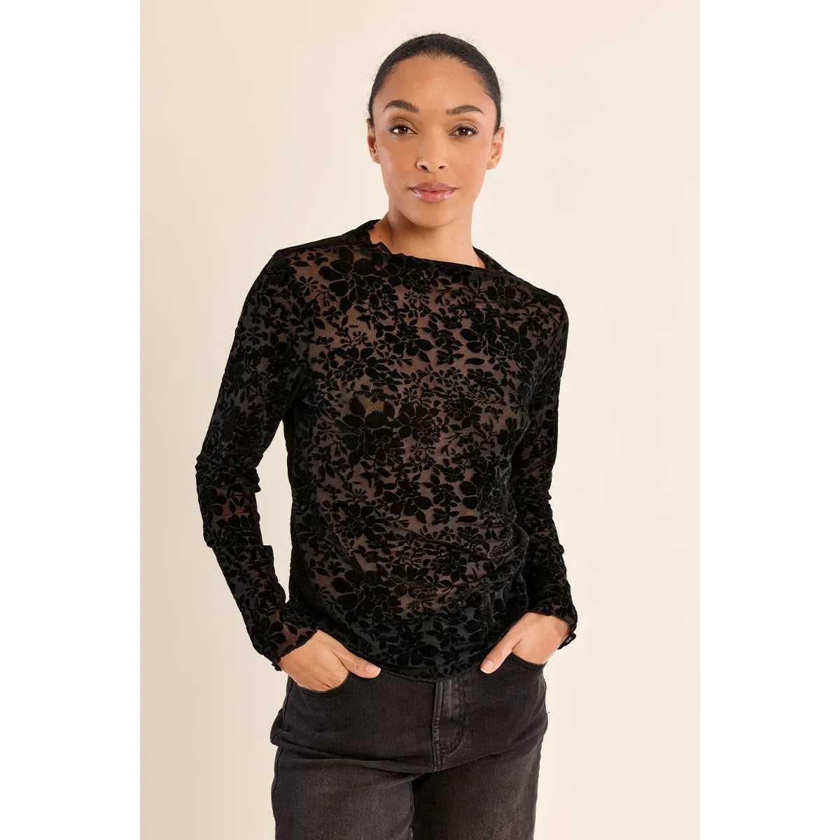 Black semi-transparent mock neck lace top with long sleeves and floral pattern, styled with dark jeans.