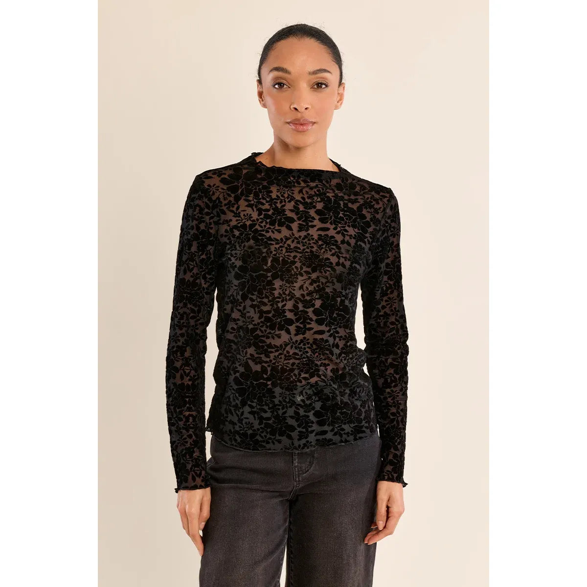 Black semi-transparent mock neck lace top with floral pattern, long sleeves, and stand-up collar worn with dark jeans.