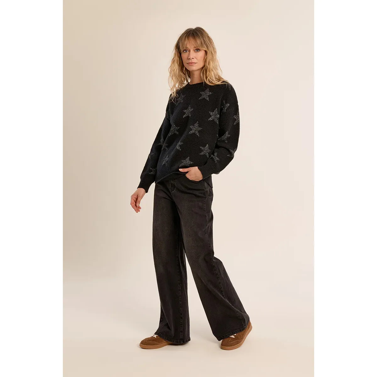 Model wearing a black glittery star knit sweater with a relaxed fit, round neckline, and long sleeves paired with dark wide-leg jeans.