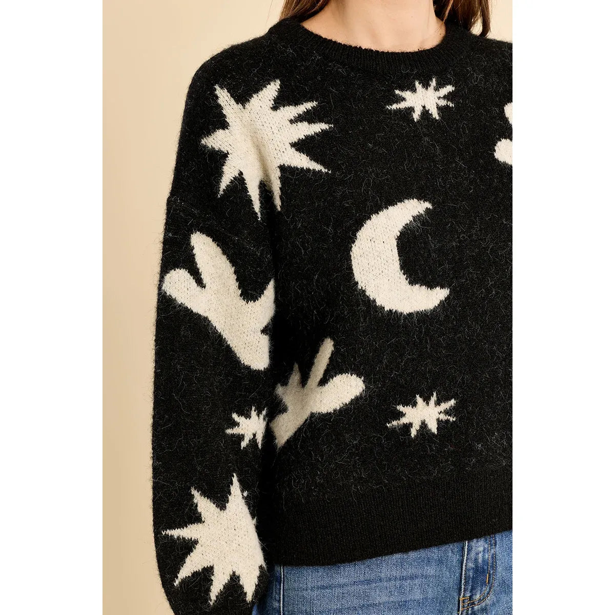Black knit sweater featuring white stars and moons, ribbed collar, and balloon sleeves. Pair with jeans for a cozy fall look.
