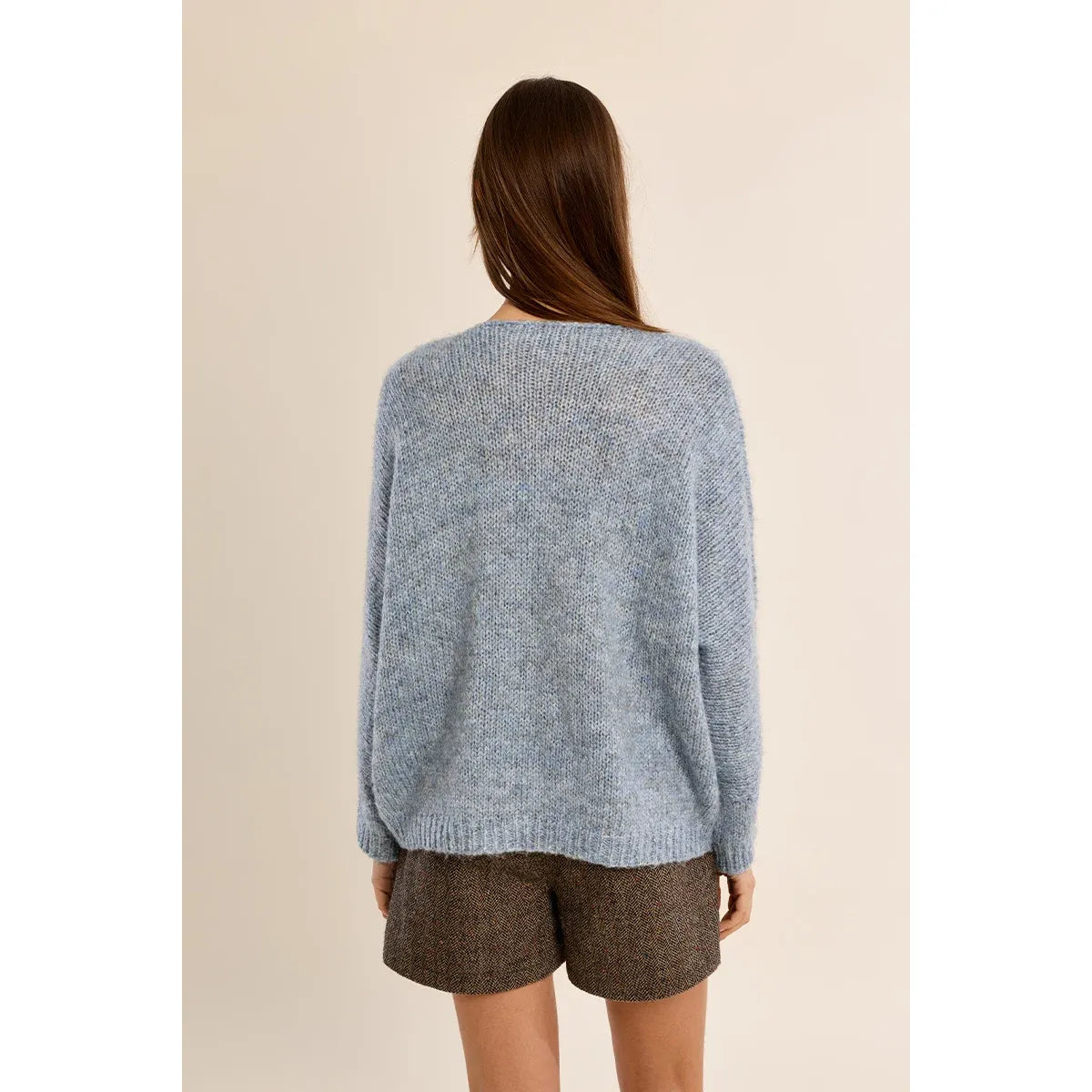 Back view of a light blue fuzzy V-neck sweater with long sleeves and straight fit, paired with brown herringbone shorts.
