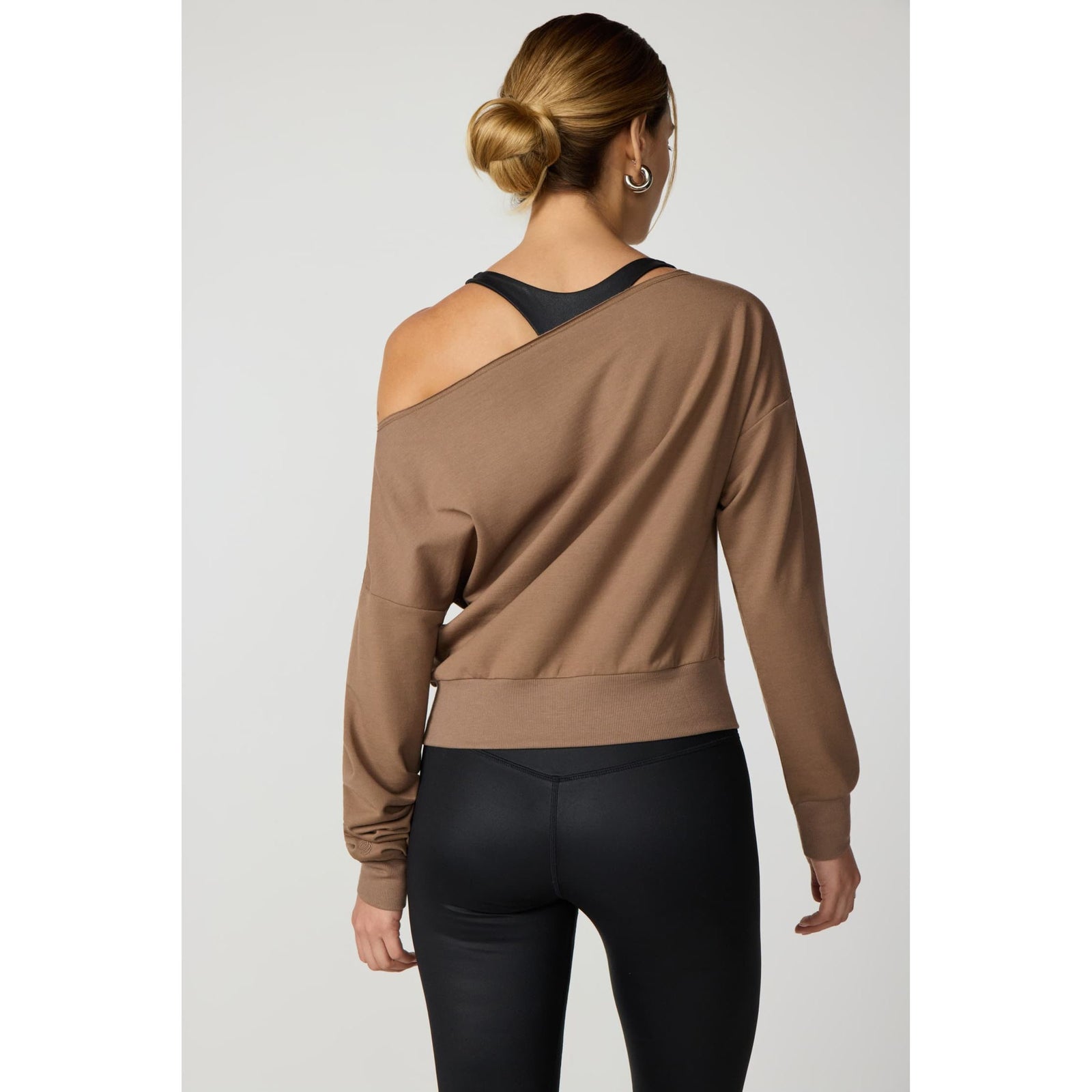 Brown off-shoulder sweatshirt with raw edge neckline, ribbed cuffs, and hem worn over black athletic tank top.