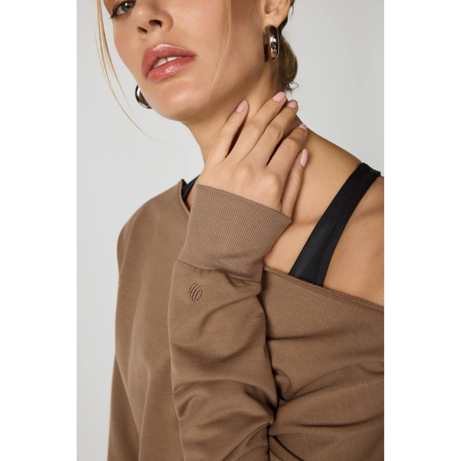 Brown cozy sweatshirt featuring raw edge neckline, ribbed cuffs, and a small embroidered logo on the sleeve.