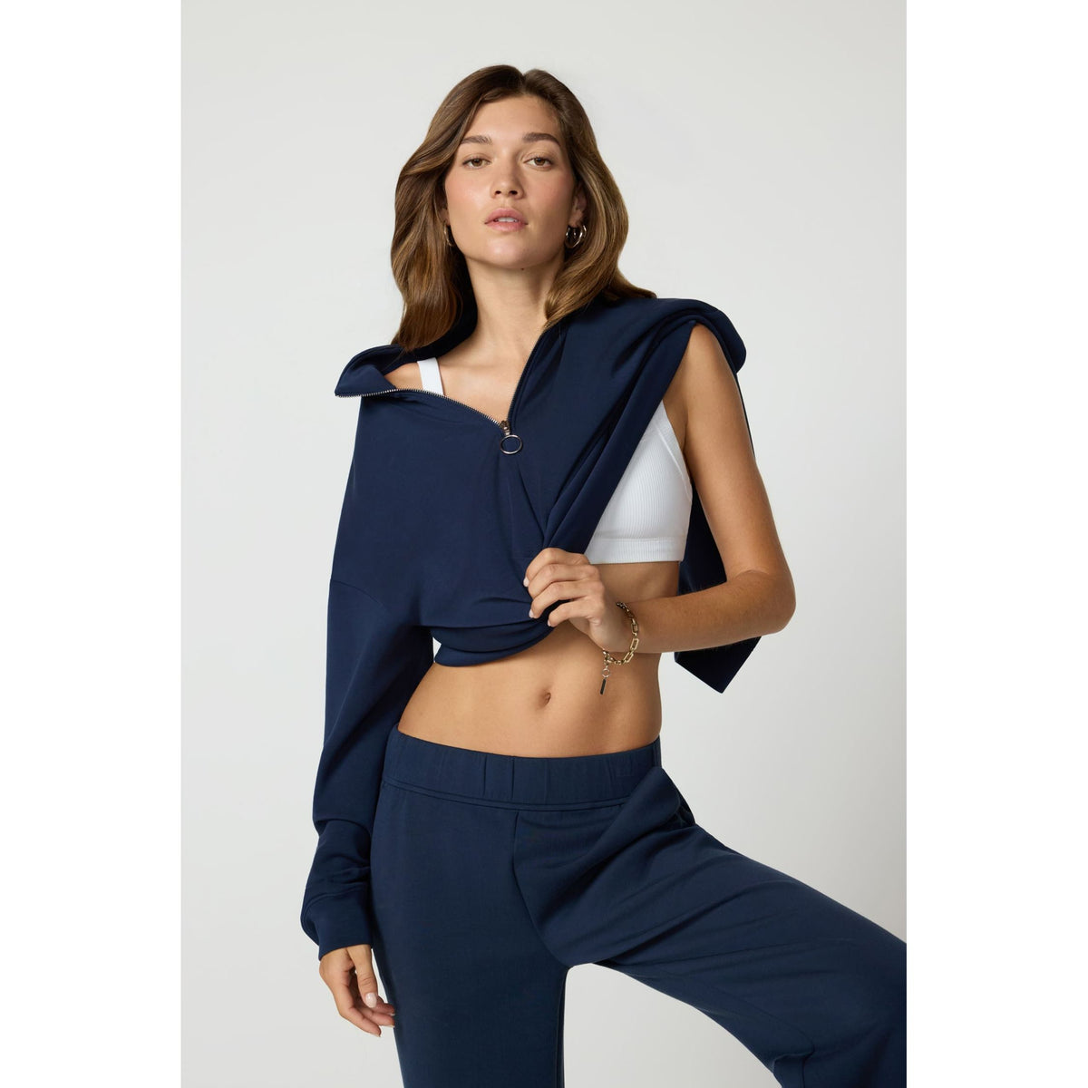 Navy blue crossover quarter-zip pullover with dropped shoulders and ring zipper detail, styled over a white sports bra.
