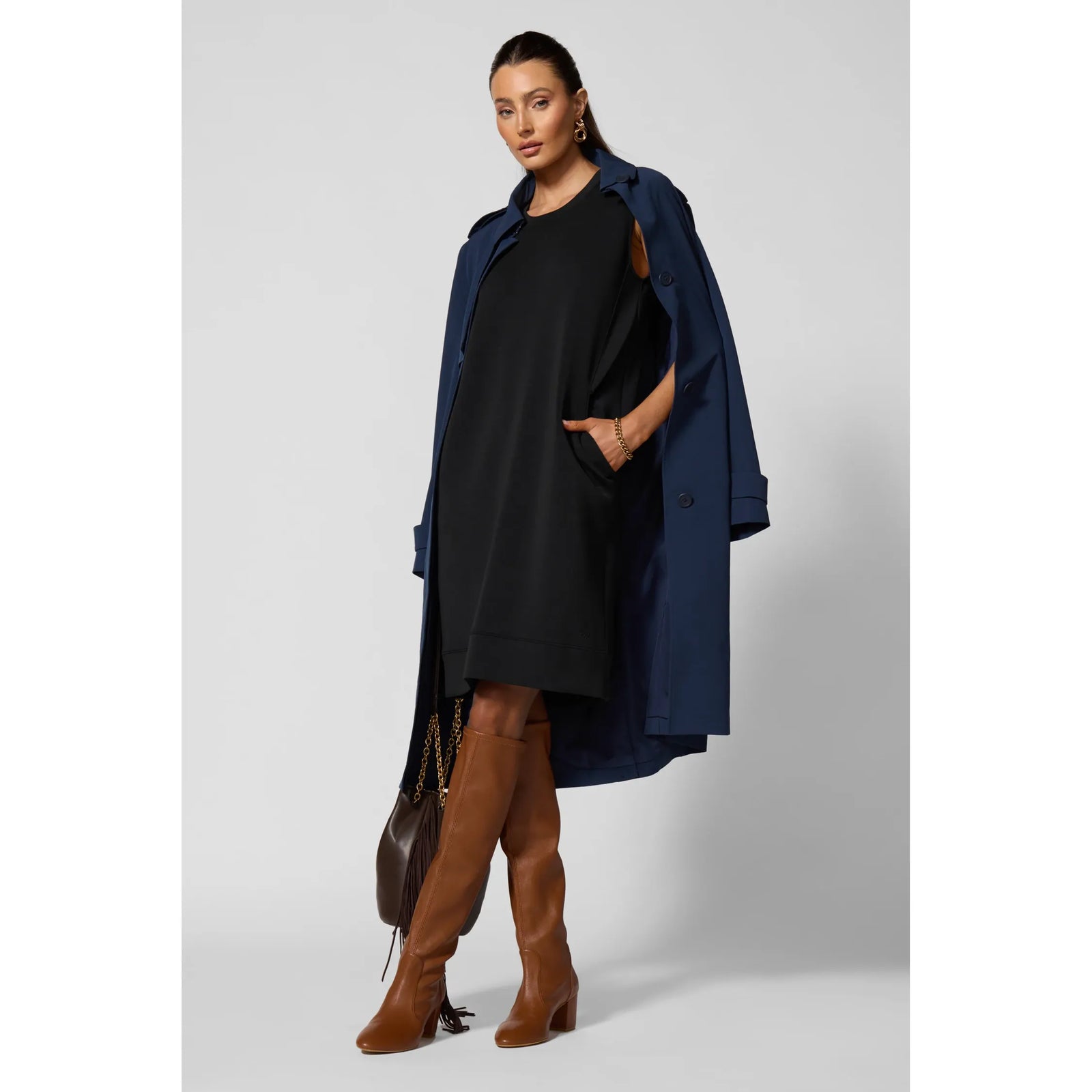 Black sleeveless dress with functional side pockets styled with a navy trench coat and brown leather over-the-knee boots.