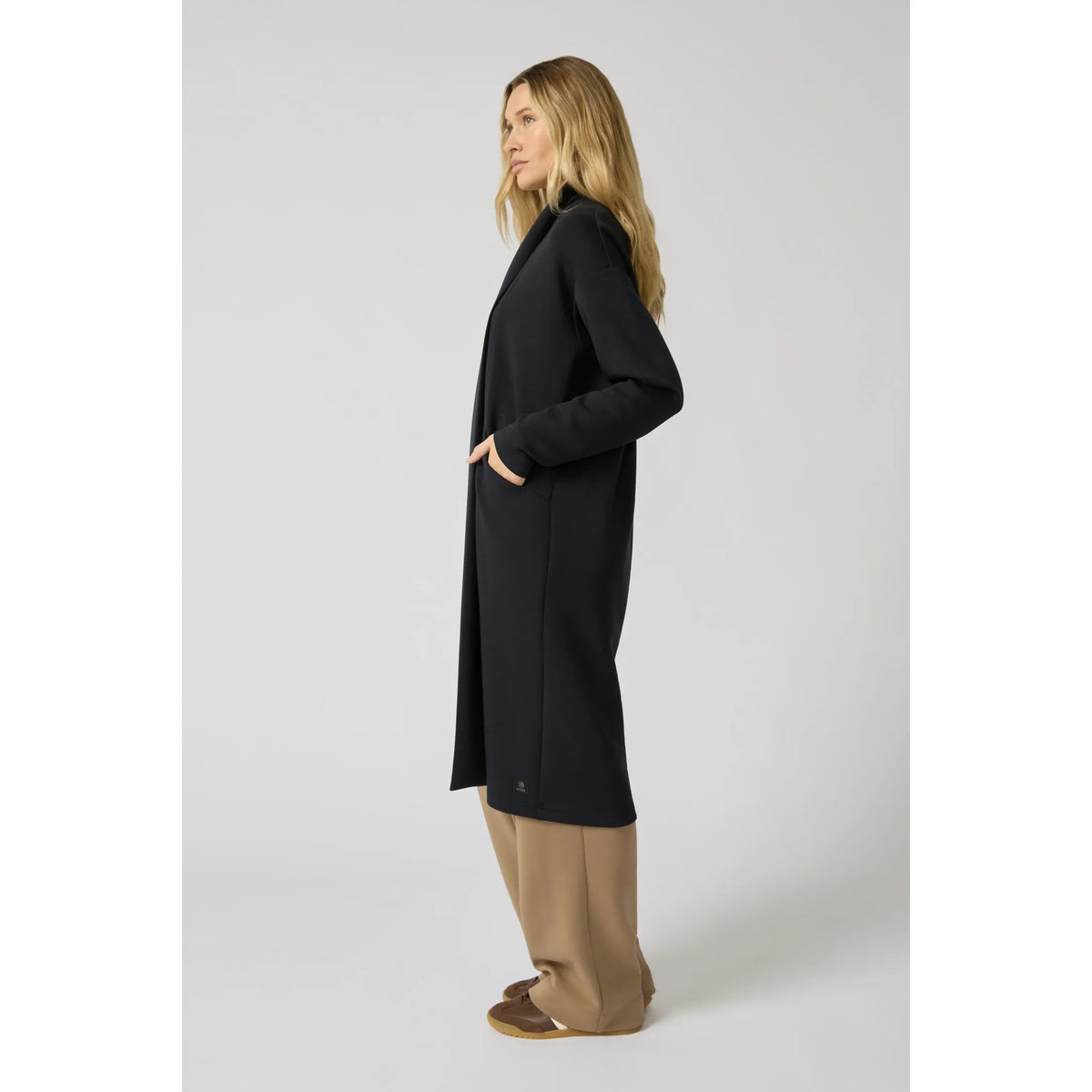 Woman wearing a black long cardigan with a clean longline silhouette, showing side profile and hand in pocket for draped comfort.