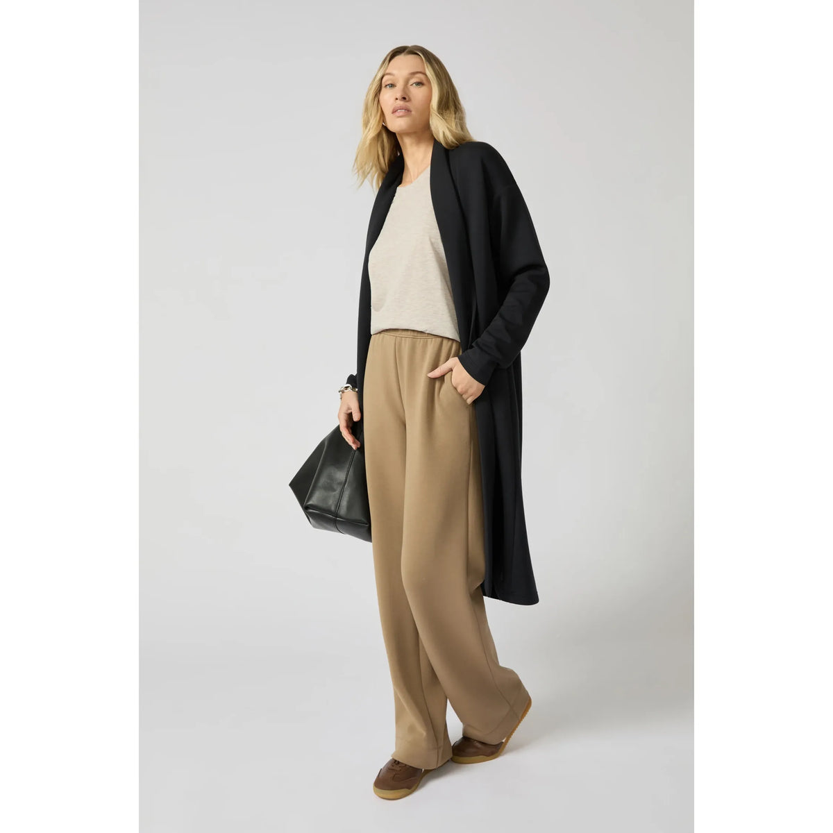 Woman wearing a black long cardigan with a clean longline silhouette over beige top and tan wide-leg pants.