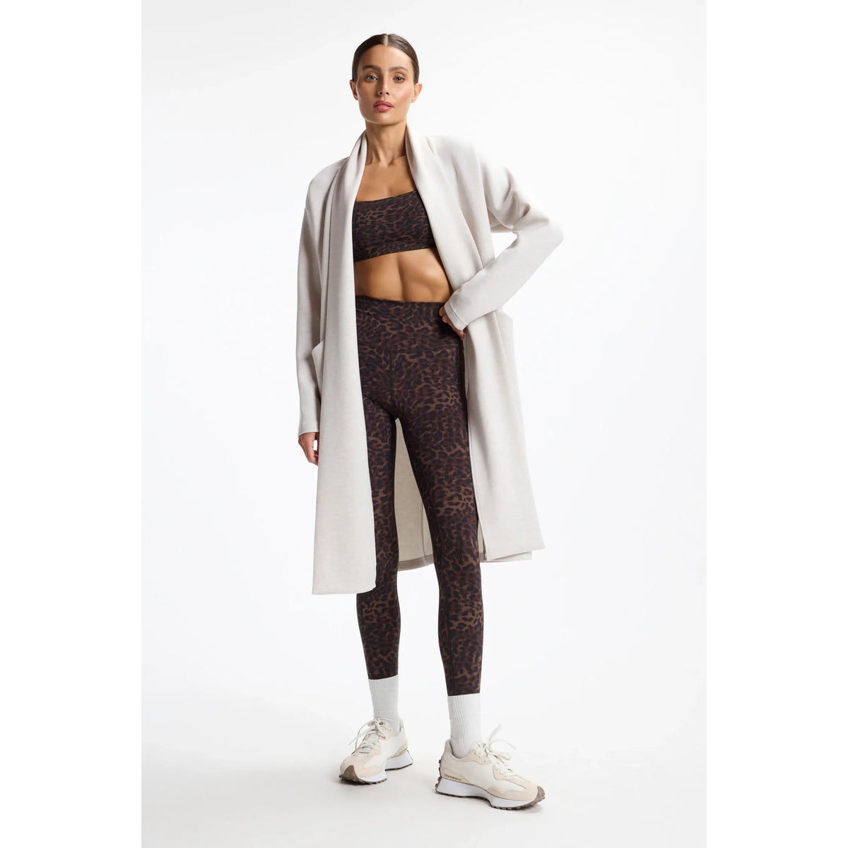Model wearing a light beige longline cardigan over a leopard print activewear set and sneakers.