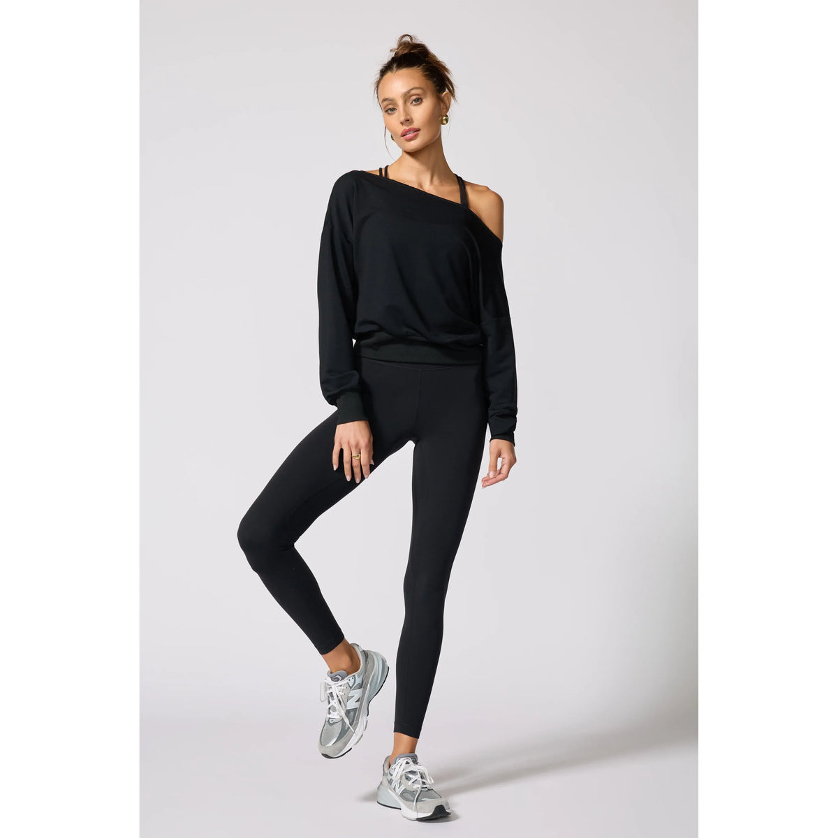 Black flashdance sweatshirt with raw edge neckline and ribbed cuffs, styled with matching leggings and sneakers for a cozy, modern look.