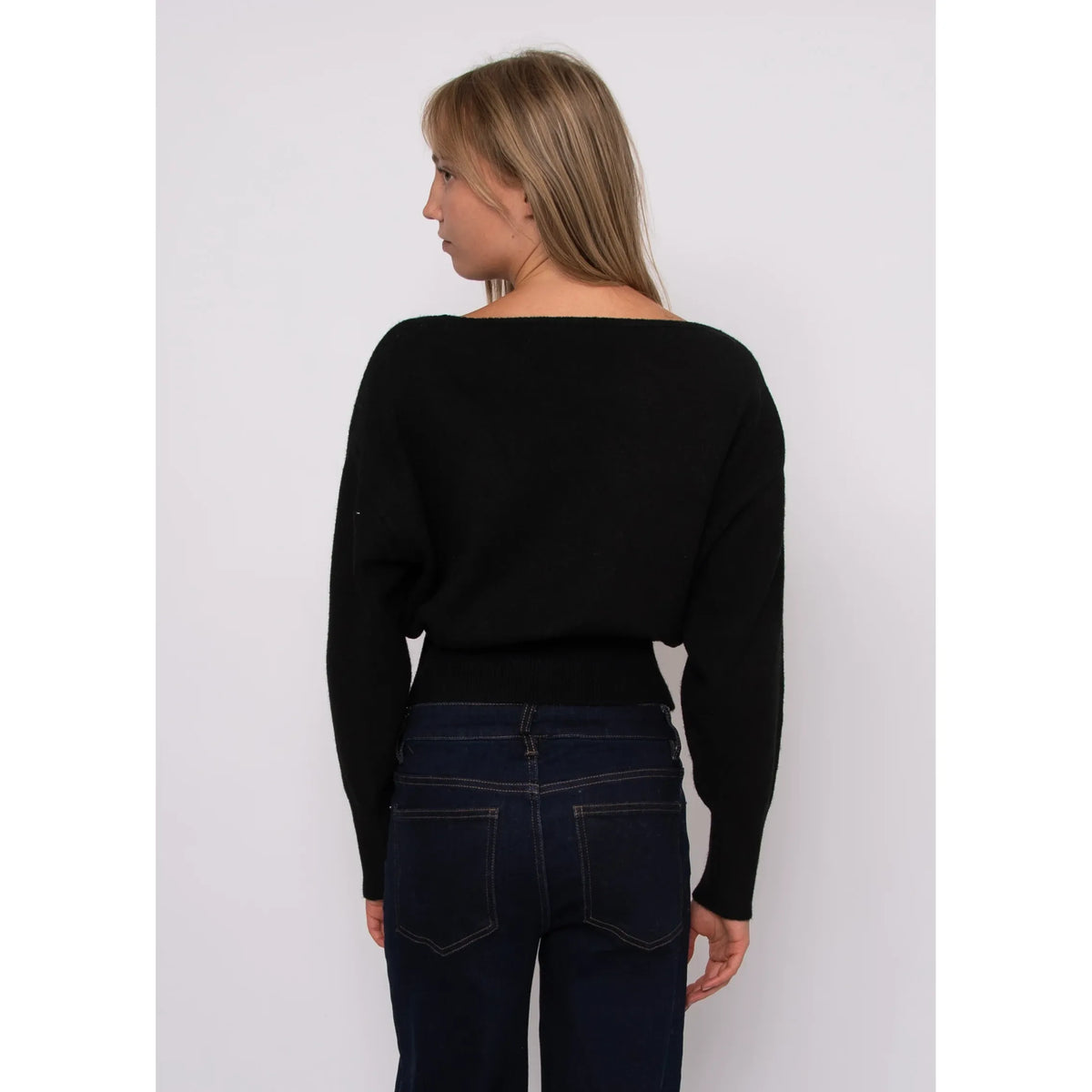 Back view of a black boat neck long sleeve sweater with a ribbed hem, paired with dark denim jeans.