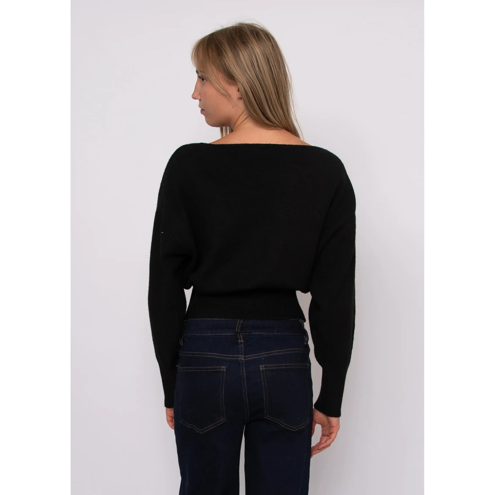 Back view of a black boat neck long sleeve sweater with a ribbed hem, paired with dark denim jeans.