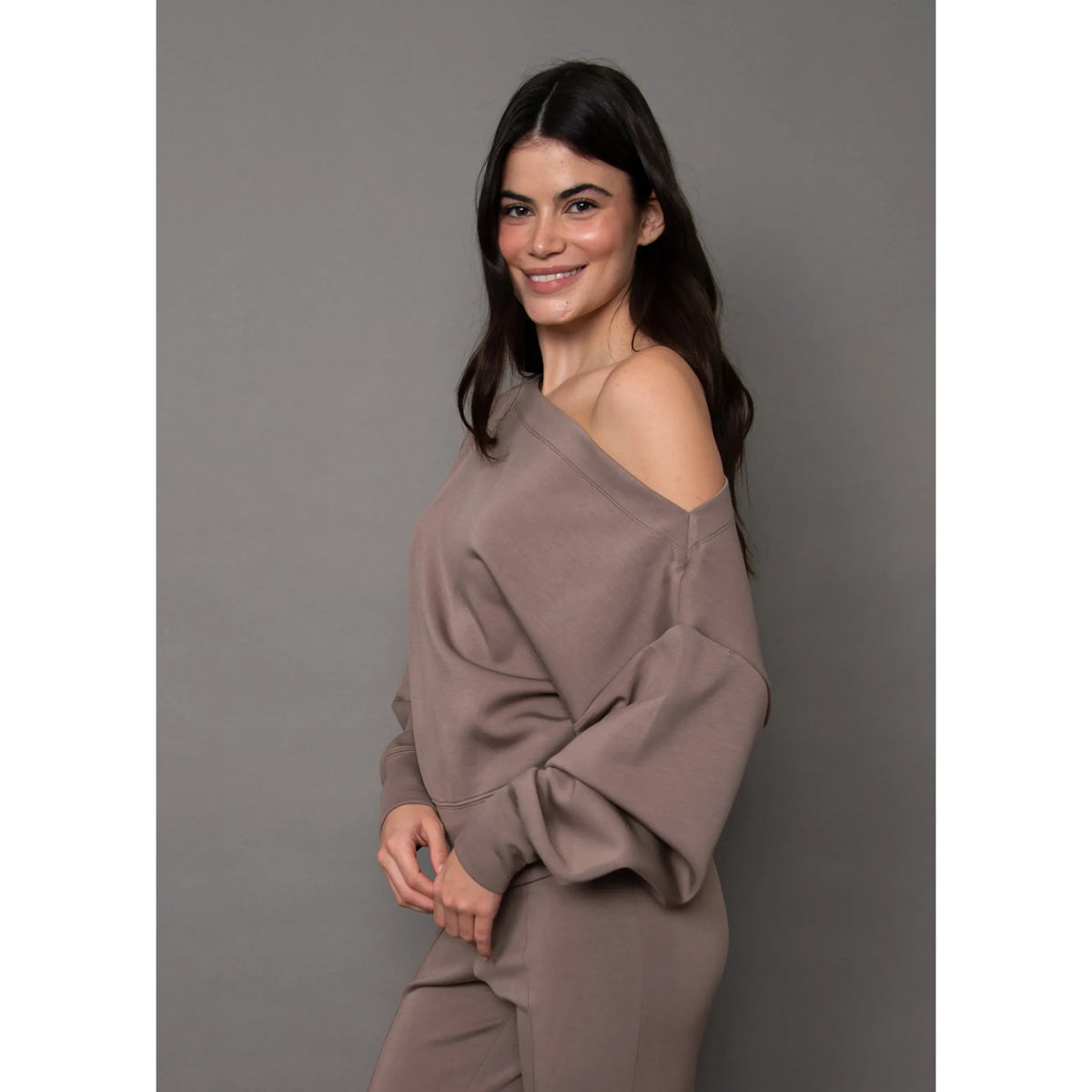Model wearing a taupe soft knit drop shoulder top with long sleeves and relaxed fit against a grey background.