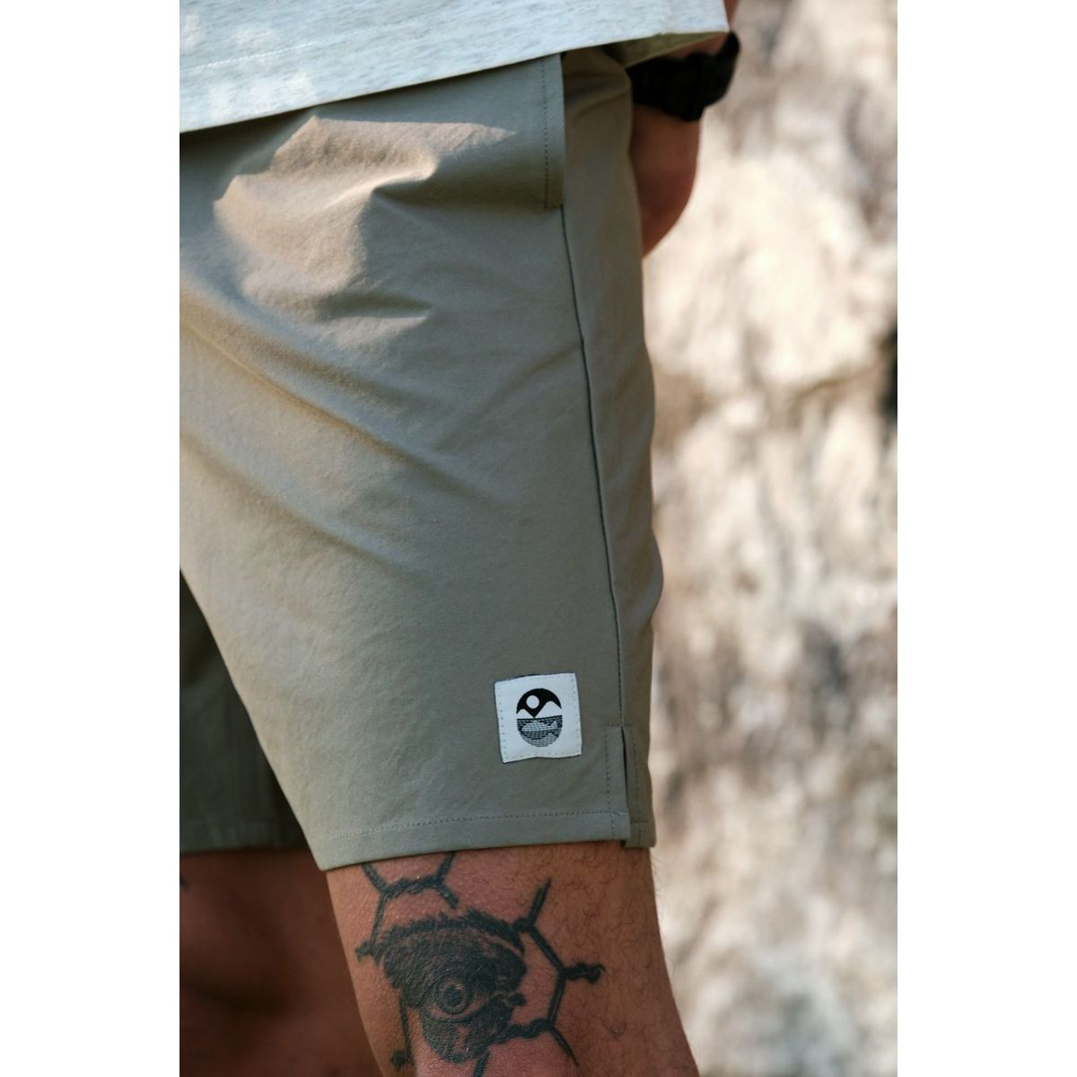 Park & Rec Nylon Shorts in khaki on a man, white logo patch at the hem and calf tattoo visible.