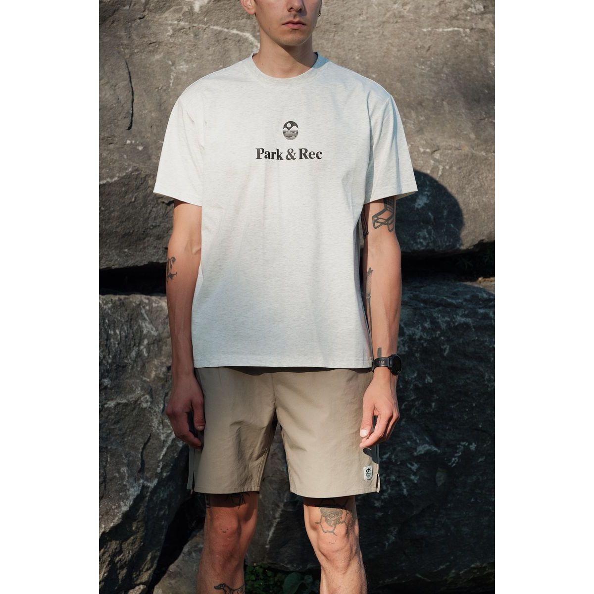 Male model wearing Park & Rec quick-dry nylon shorts in beige with a light gray tee, outdoors by rocks.