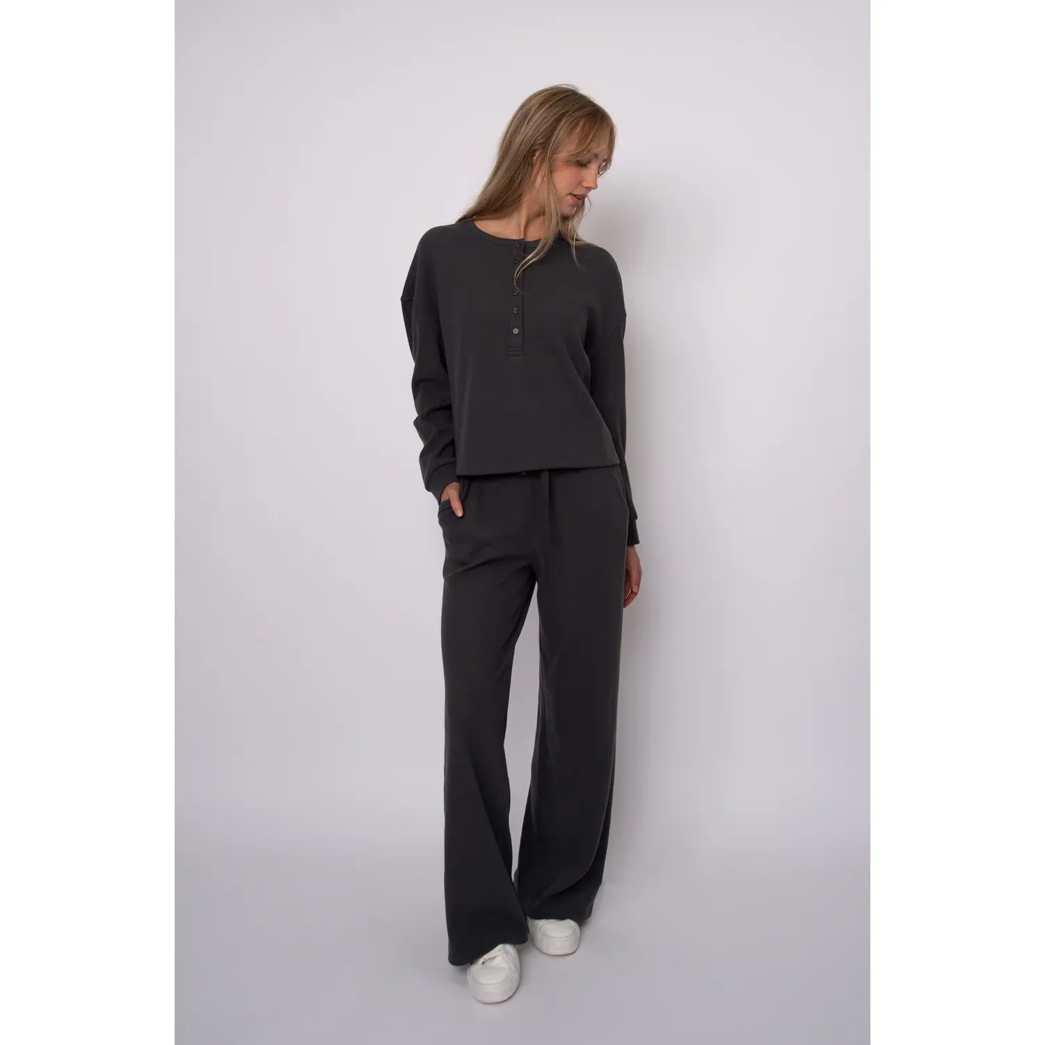 Model wearing dark grey waffle drawstring wide leg pants with a relaxed silhouette, paired with a matching long-sleeve henley top and white sneakers.