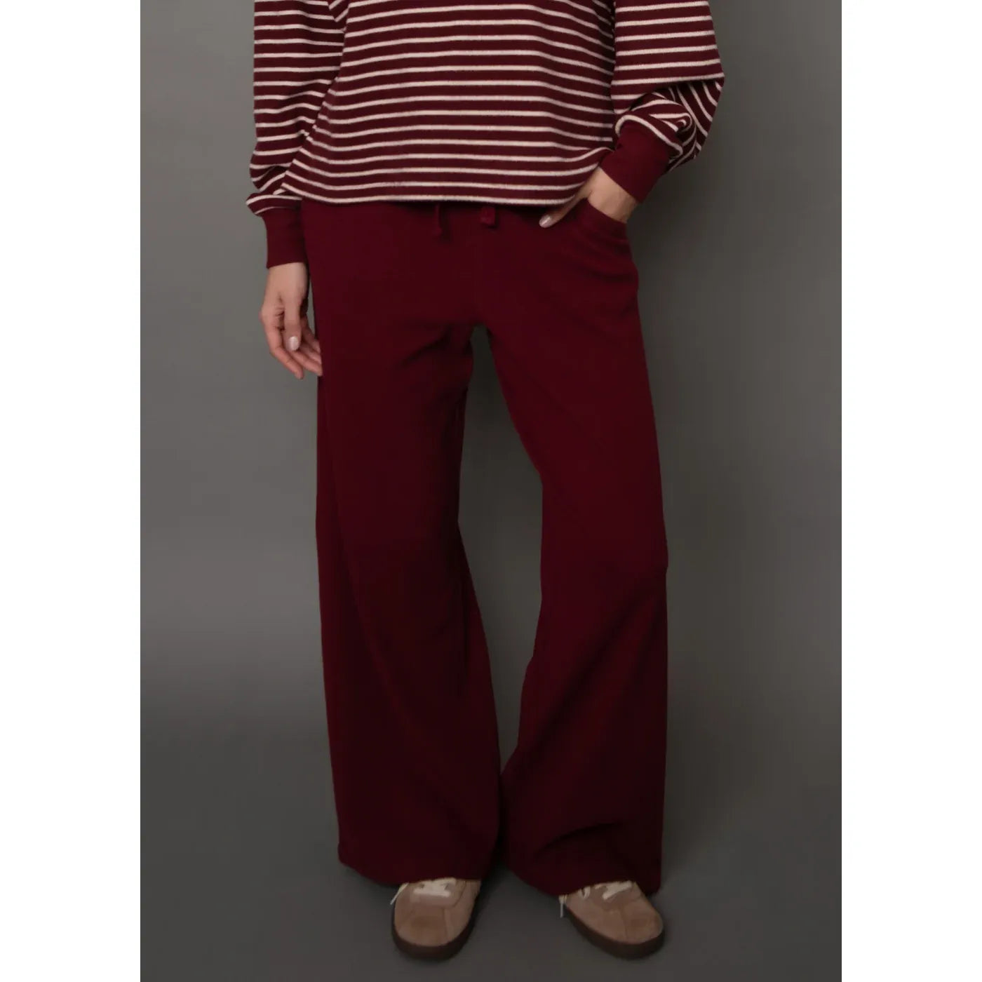 Burgundy waffle-knit wide-leg drawstring pants paired with a striped long-sleeve top and neutral sneakers.