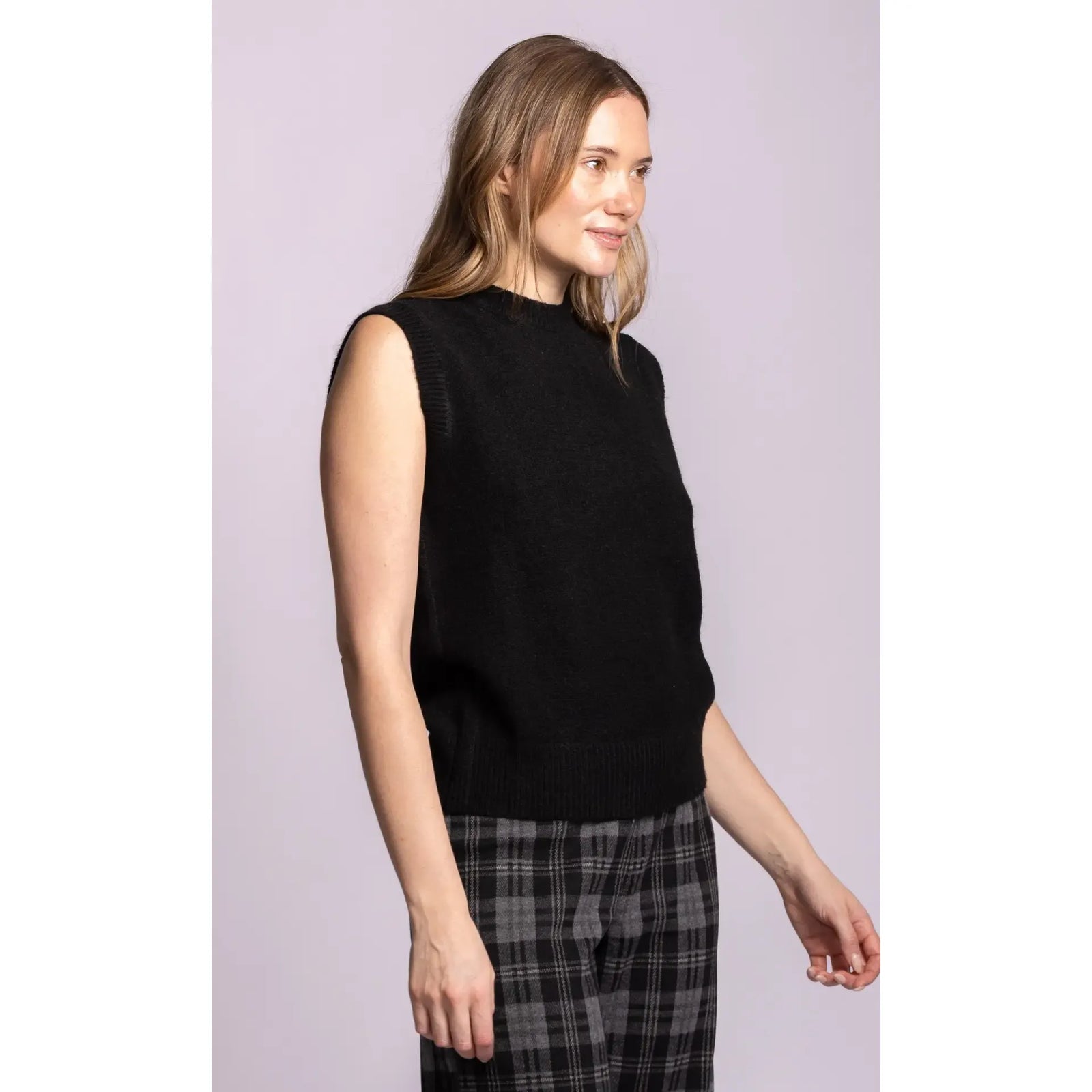 Black sleeveless ribbed sweater with structured shoulders and hem, styled with plaid trousers.