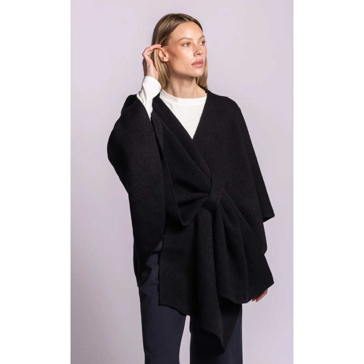 Model wearing black Lennon wrap sweater with asymmetric hem and adaptable waist tie, styled open over white top.