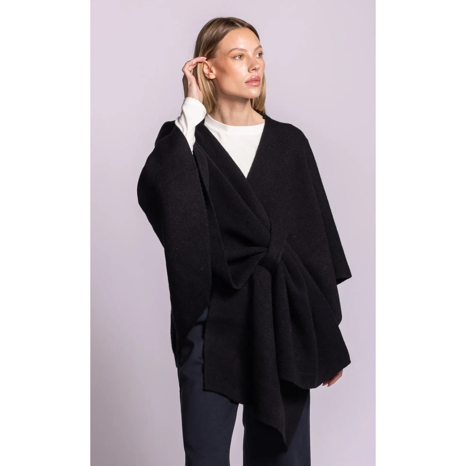 Model wearing black Lennon wrap sweater with asymmetric hem and adaptable waist tie, styled open over white top.