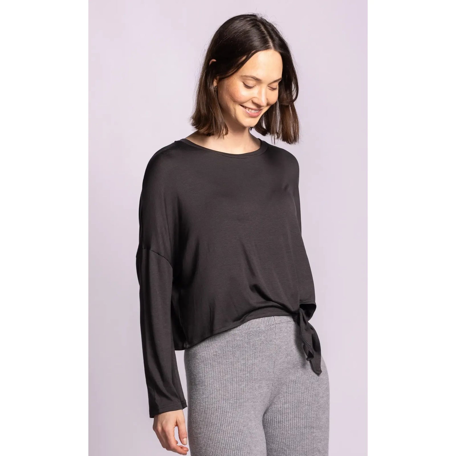 Woman wearing a dark grey Lenova Top with dropped shoulders, lightweight drape, and side self-tie detail paired with grey knit pants.