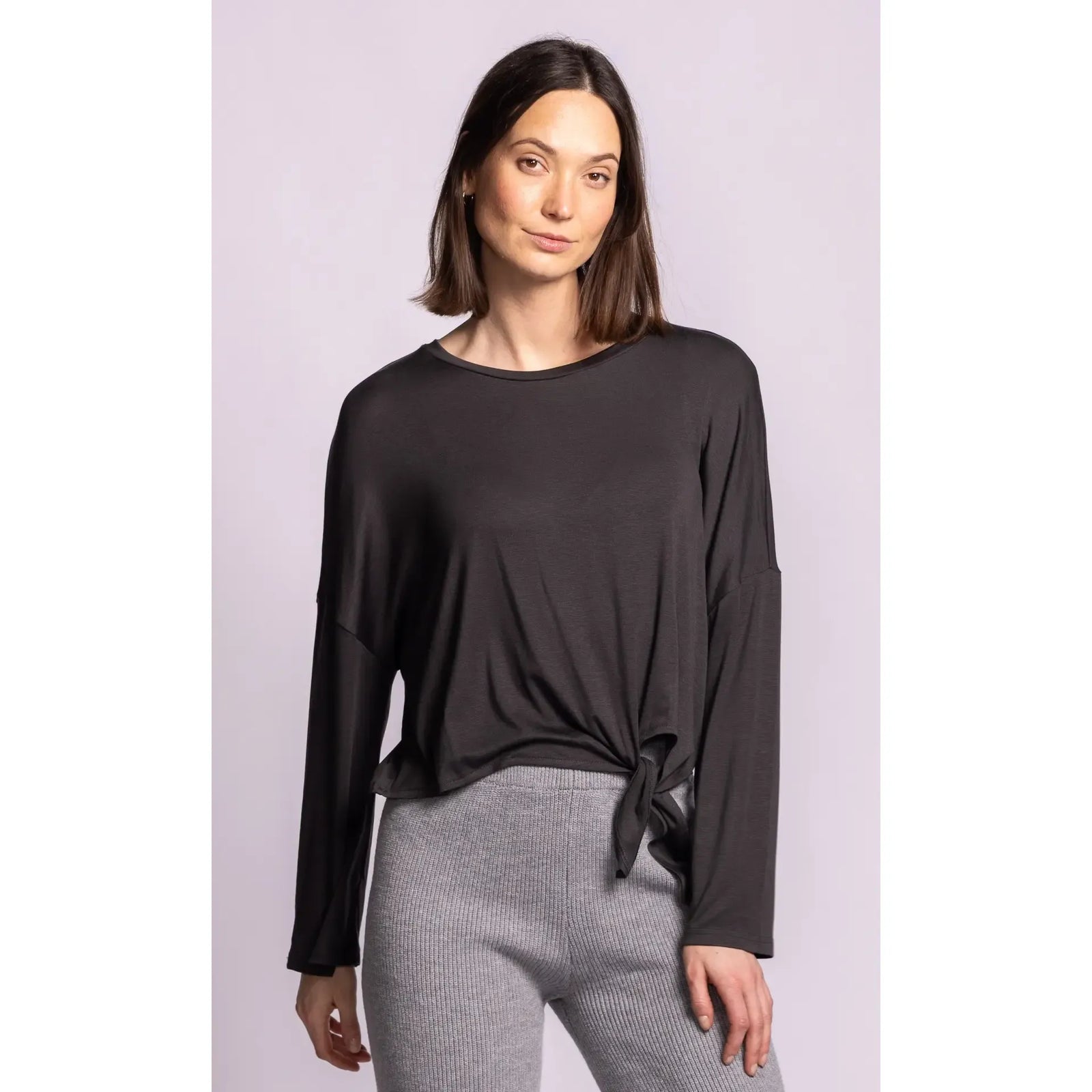 Model wearing a soft black long sleeve top featuring relaxed dropped shoulders and a charming side self-tie knot detail for effortless style.