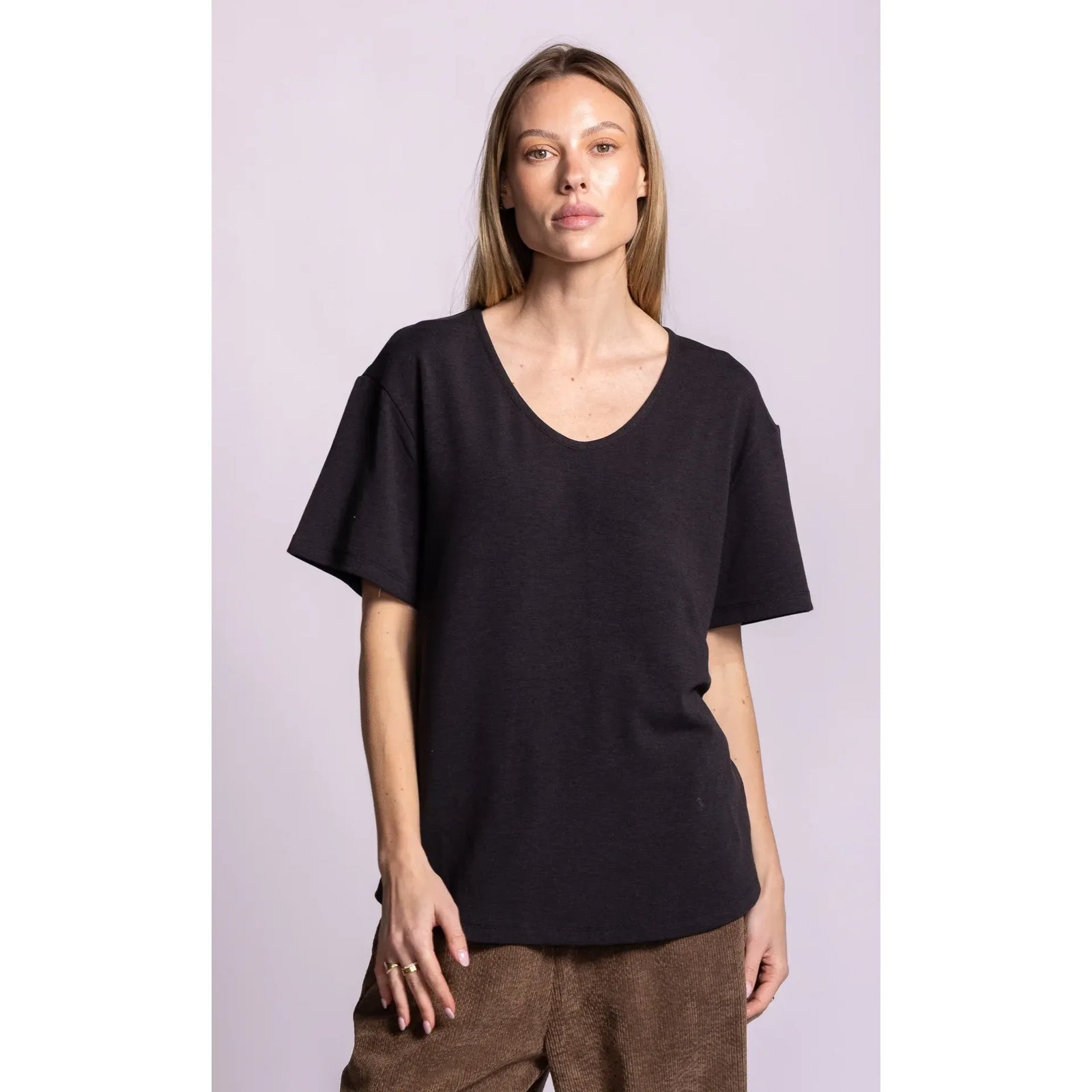 Model wears a black relaxed fit scoop neck top with dropped shoulders and short sleeves, featuring a cozy brushed lining for comfort.