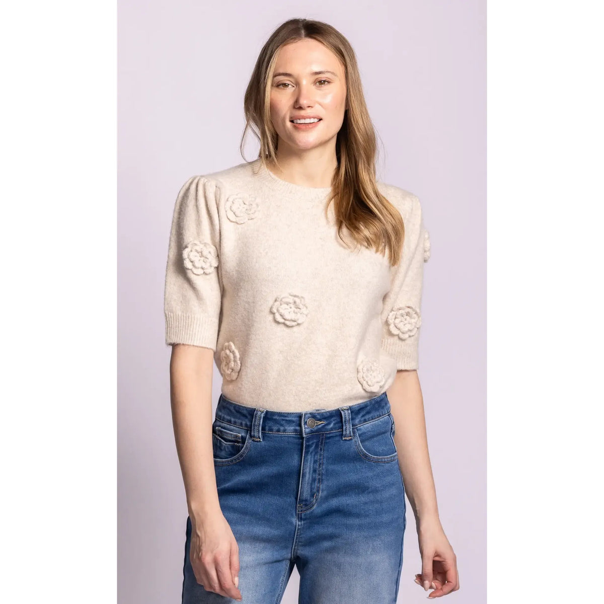 Pink Martini Roslyn sweater in cream knit with 3D rosette details, puff sleeves, and ribbed trim paired with blue jeans.