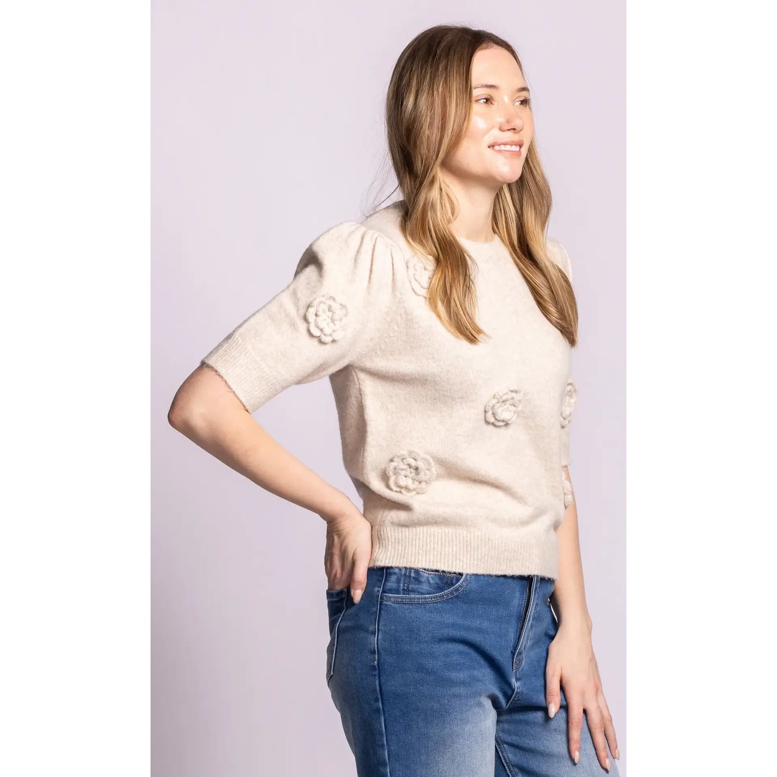 Beige Roslyn knit sweater with 3D rosette details, puff sleeves, and ribbed trim paired with blue jeans.