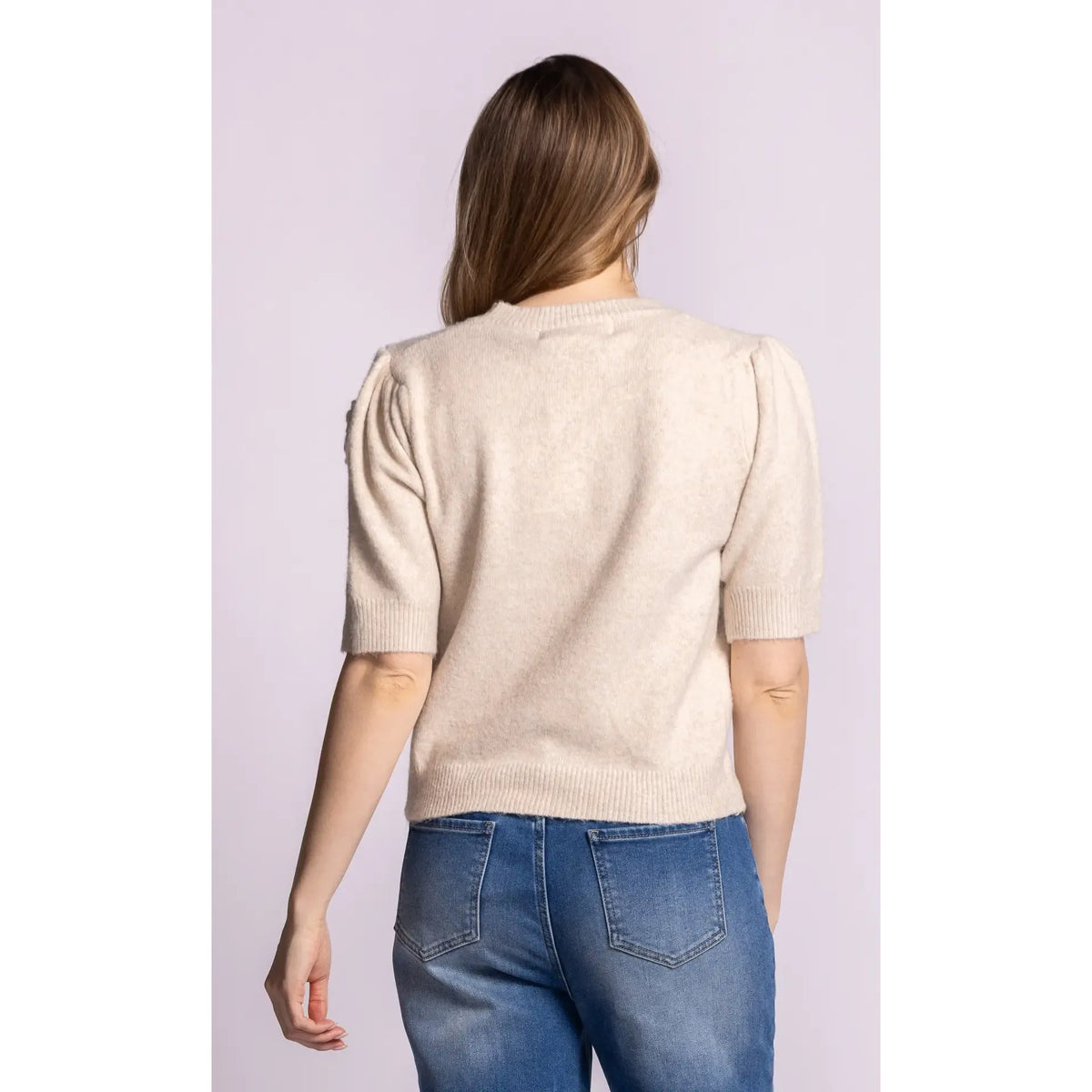 Back view of a beige knit sweater featuring puffed short sleeves, ribbed trim, and a cozy fit paired with blue jeans.