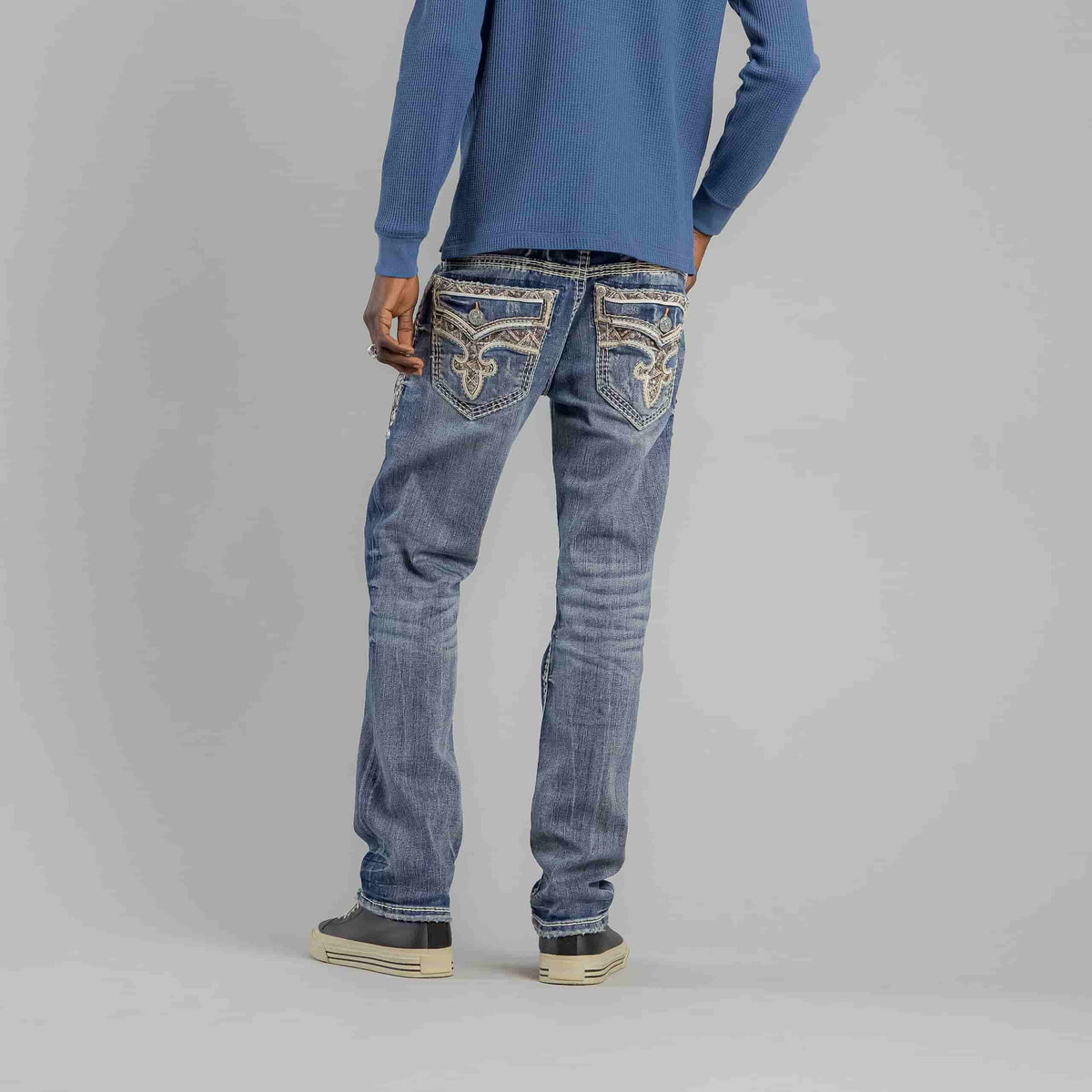 Model wearing Rock Revival Brayen J246 Straight jeans with ornate back pockets and a blue sweater.