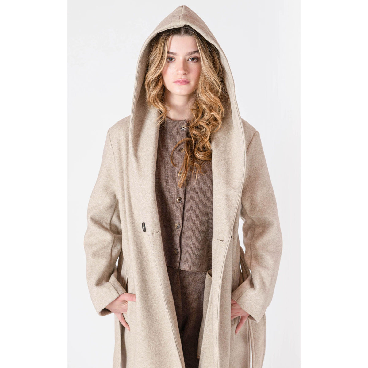 Room 34 Belted Hooded Coat worn by a model; long beige coat with oversized hood, belt and front button closure.