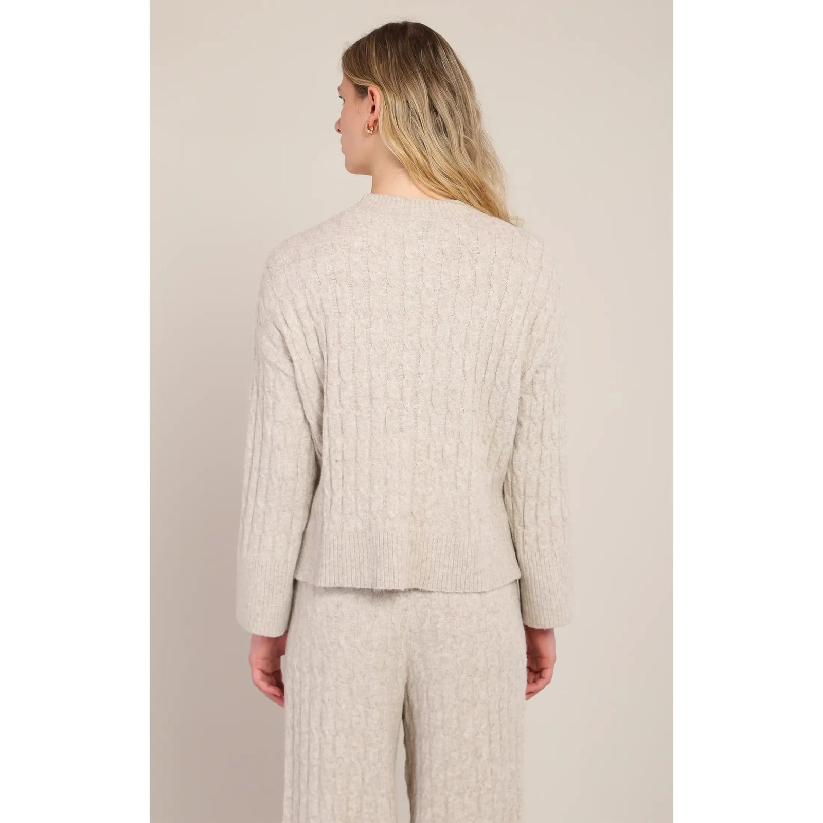 Back view of beige cable knit sweater with crew neck and matching pants, showcasing cozy wool blend texture for cold weather.