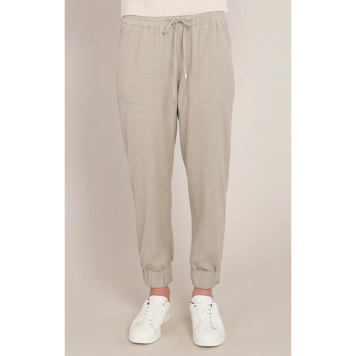 Beige knit cuffed hem pants with drawstring waist, relaxed fit, and white sneakers for a chic casual look.