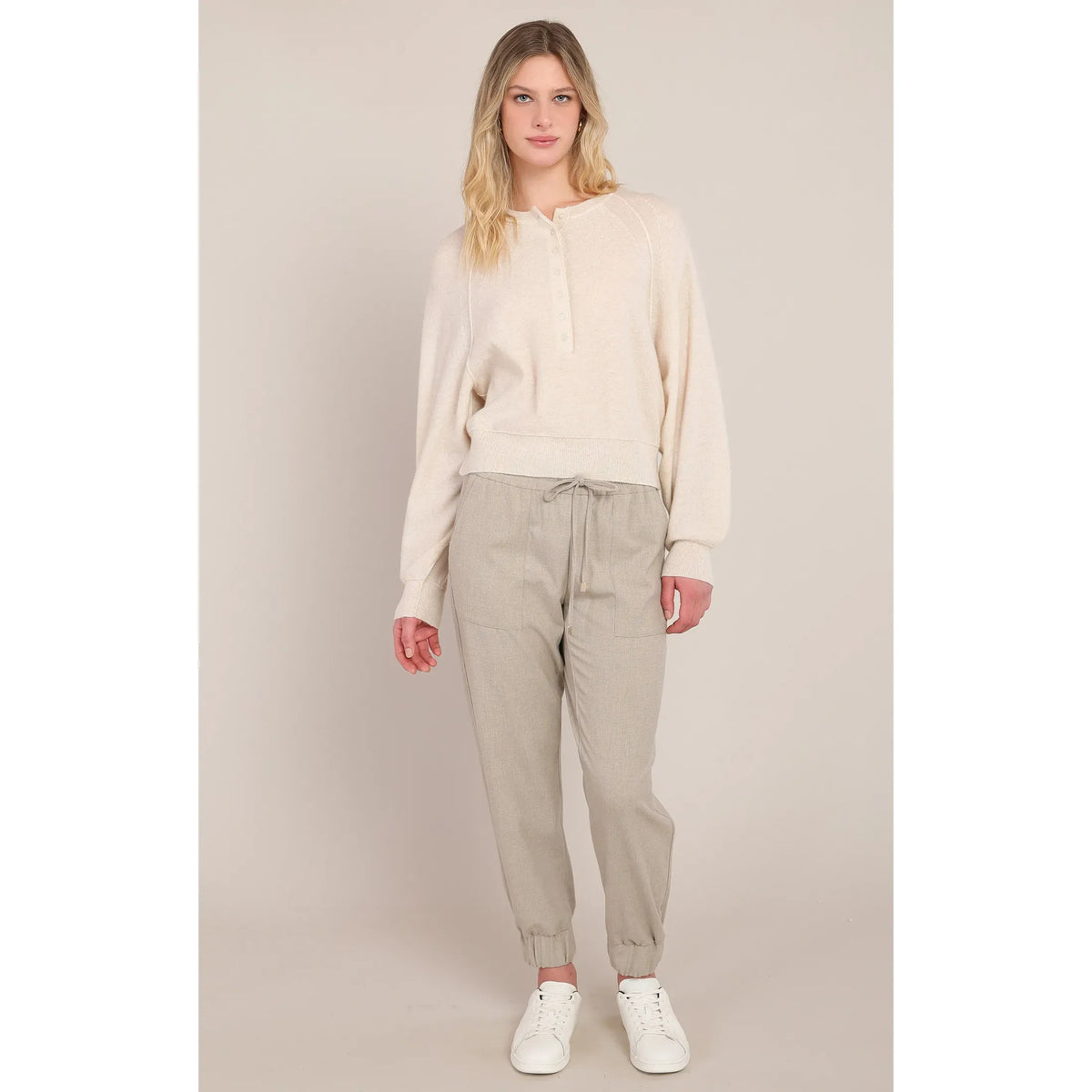 Model wearing beige cuffed hem pants with a drawstring waist and relaxed fit, styled with a cream sweater and white sneakers.