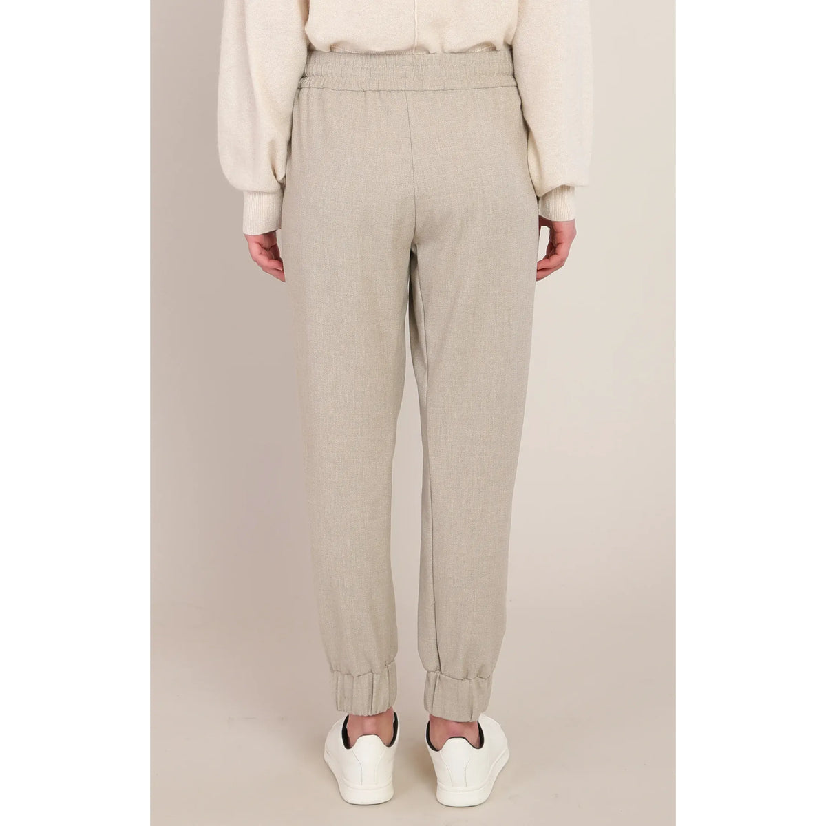 Back view of beige cuffed hem knit pants with a relaxed fit and elastic waistband, styled with white sneakers.